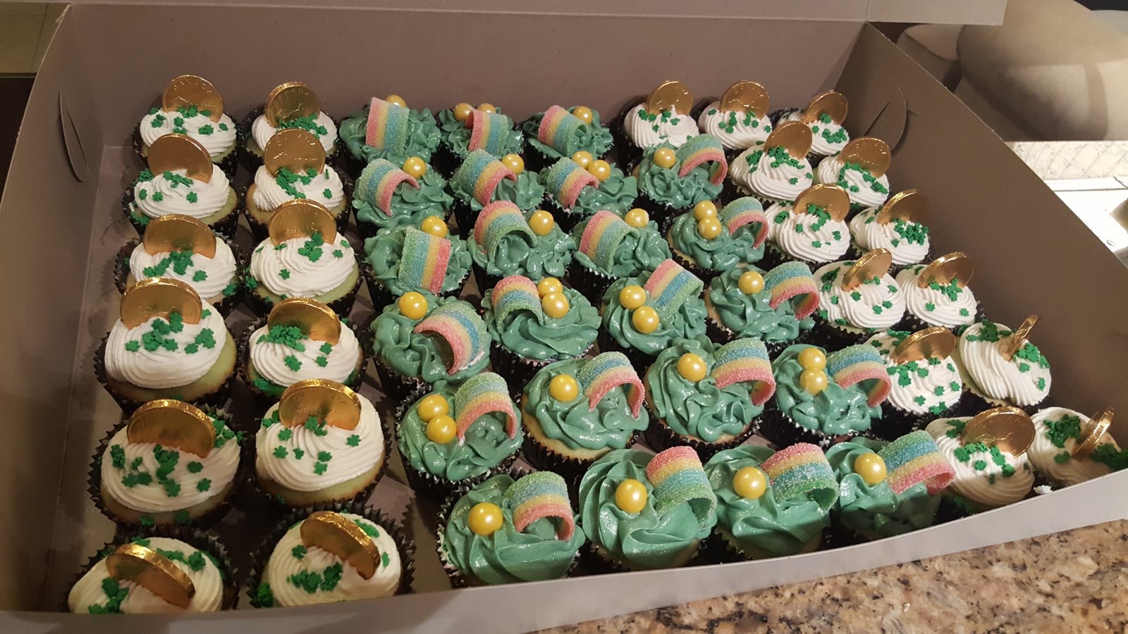 Box of St. Patrick's Day cupcakes with gold coins, shamrock sprinkles, and candy rainbows