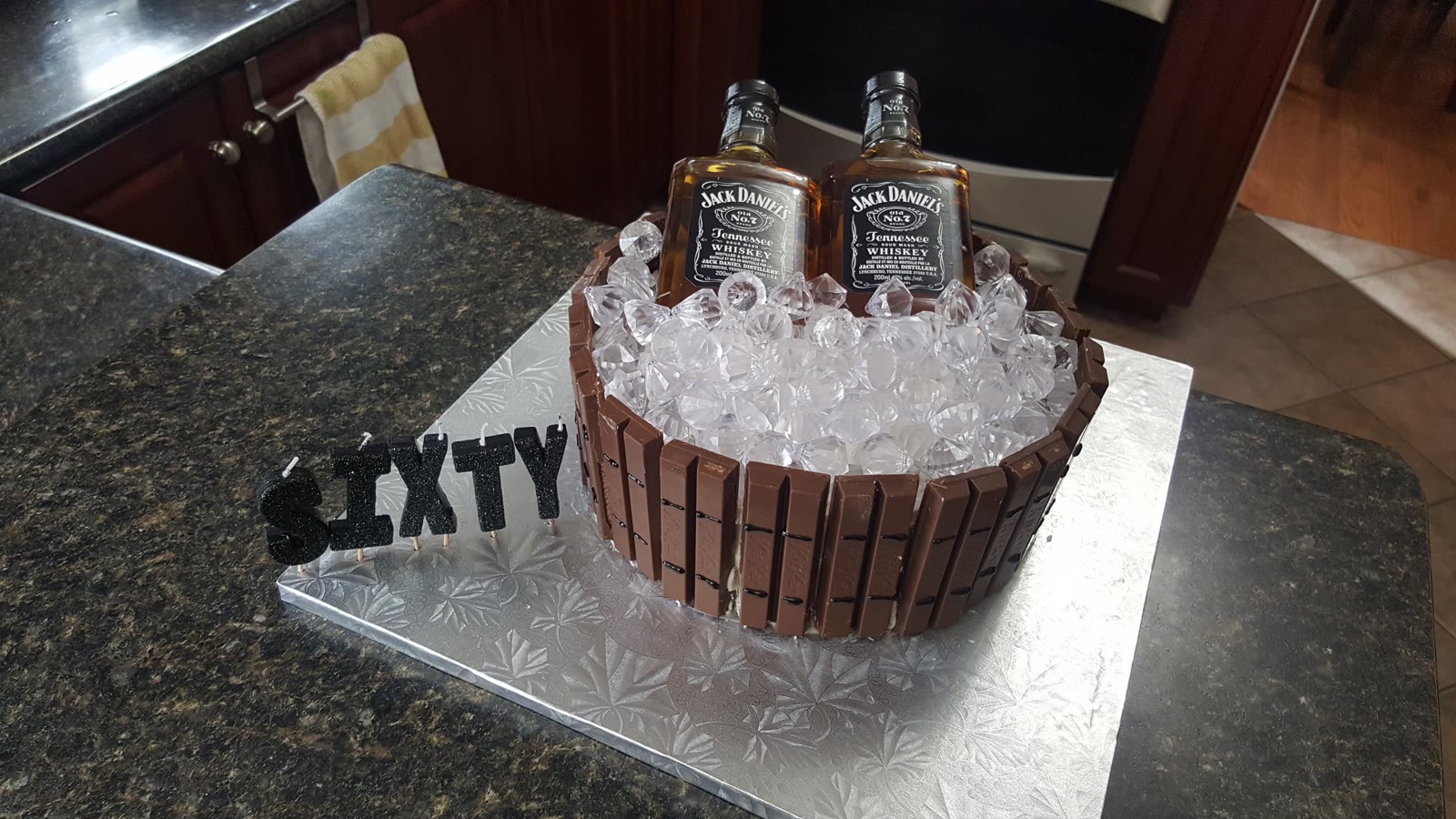 Sixtieth birthday cake ringed with Kit Kats and topped with ice-style gems and two mini whiskey bottles