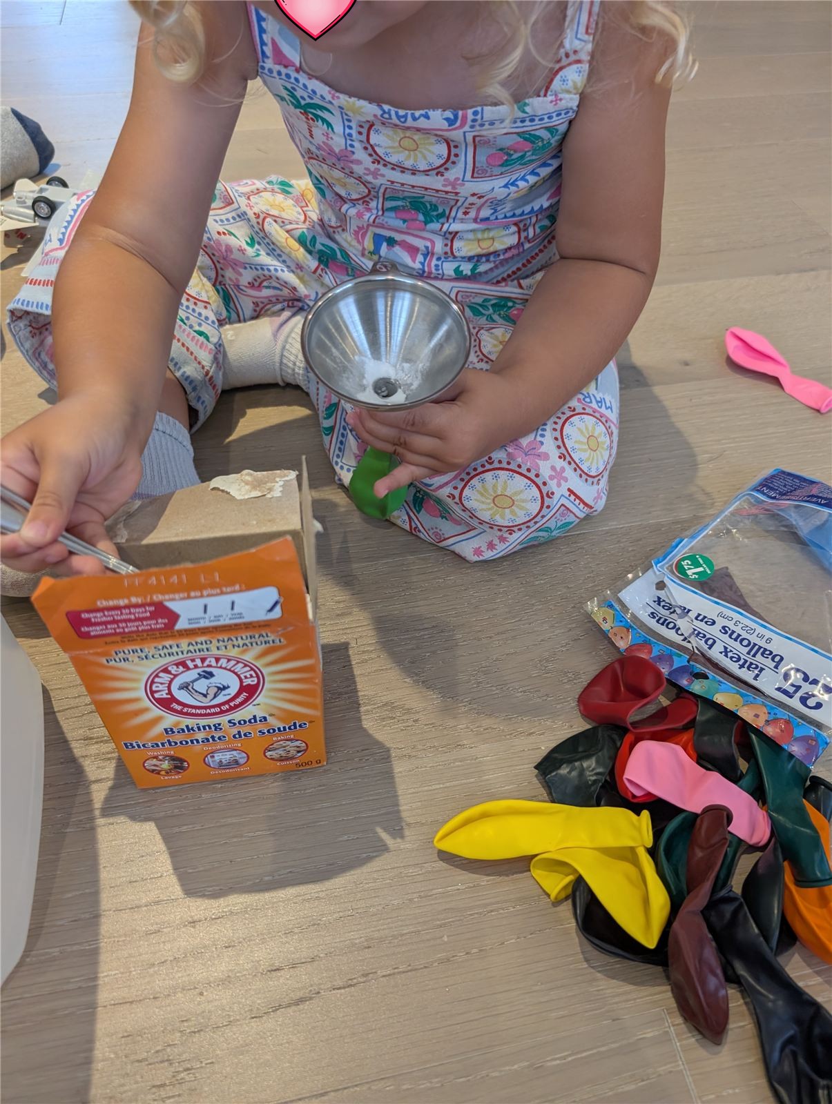 Child using a funnel to pour baking soda into a balloon