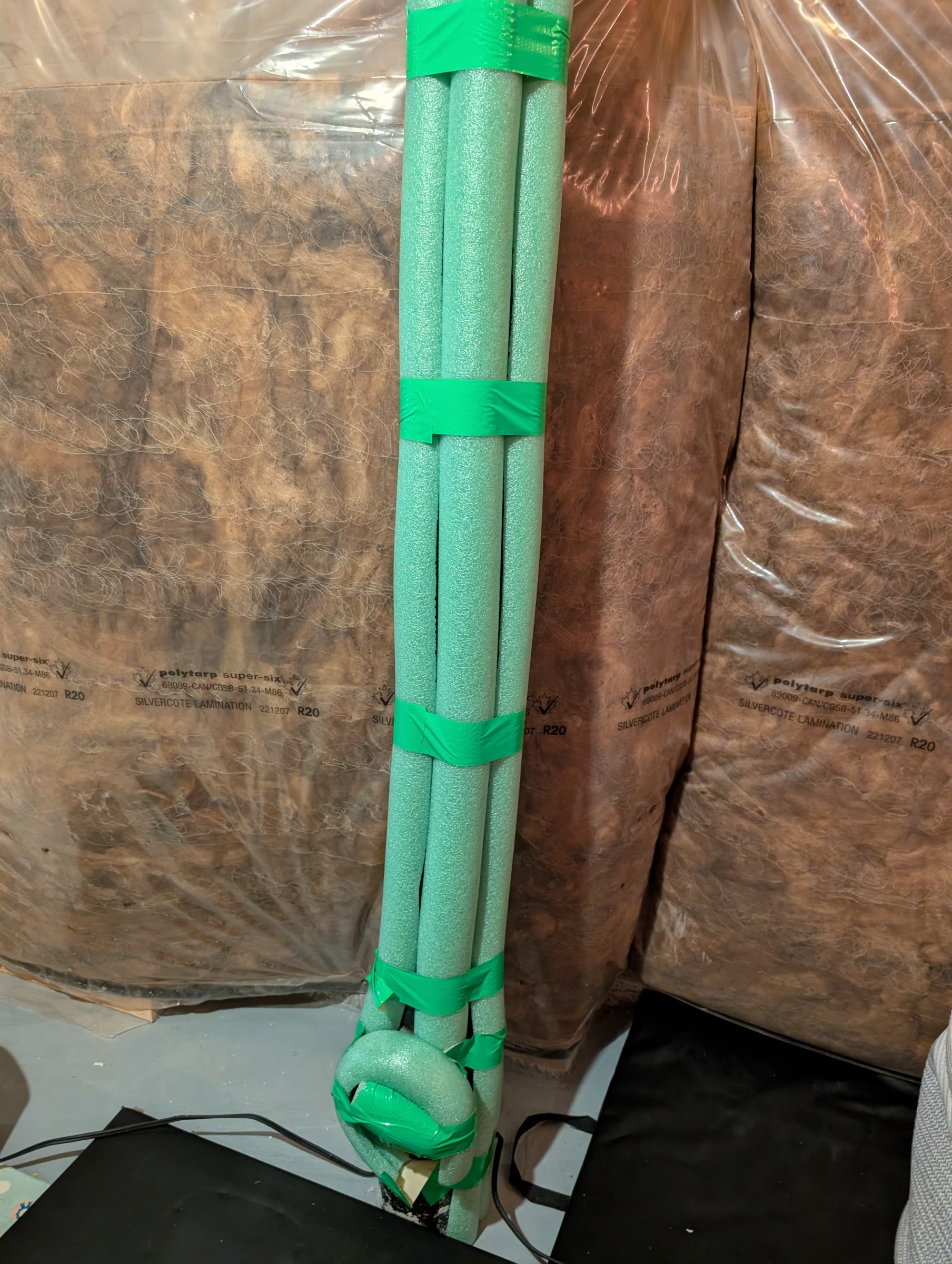 Green pool noodles cut in half and taped around an exposed pipe in the basement