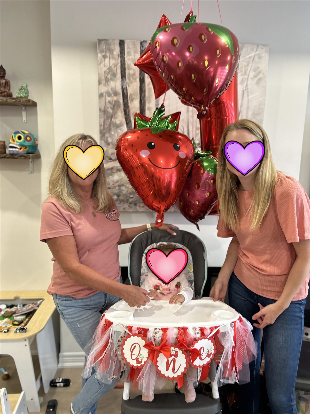 Birthday girl in a decorated high chair with strawberry balloons, flanked by two smiling women