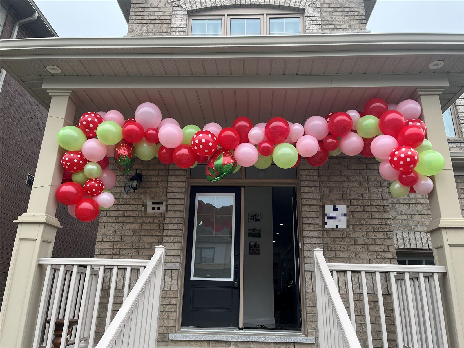 Homemade strawberry-themed balloon garland over a front porch