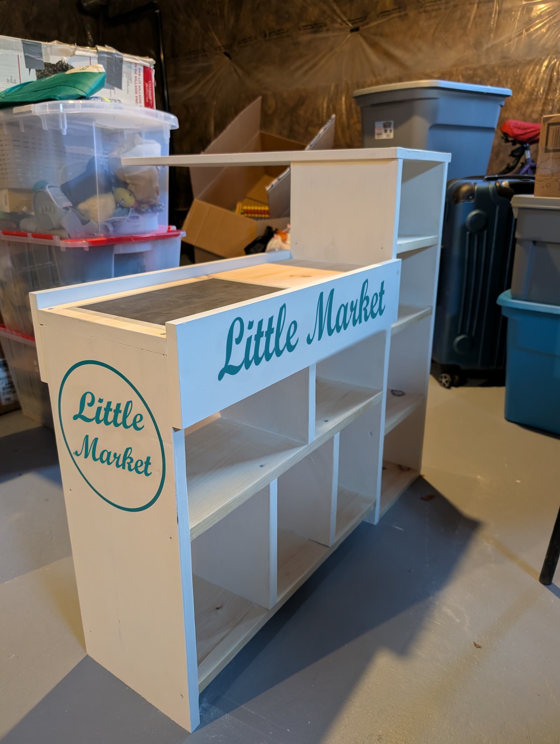 Painted white checkout counter with teal Little Market stickers on the side and front, and a dark painted conveyor belt on top