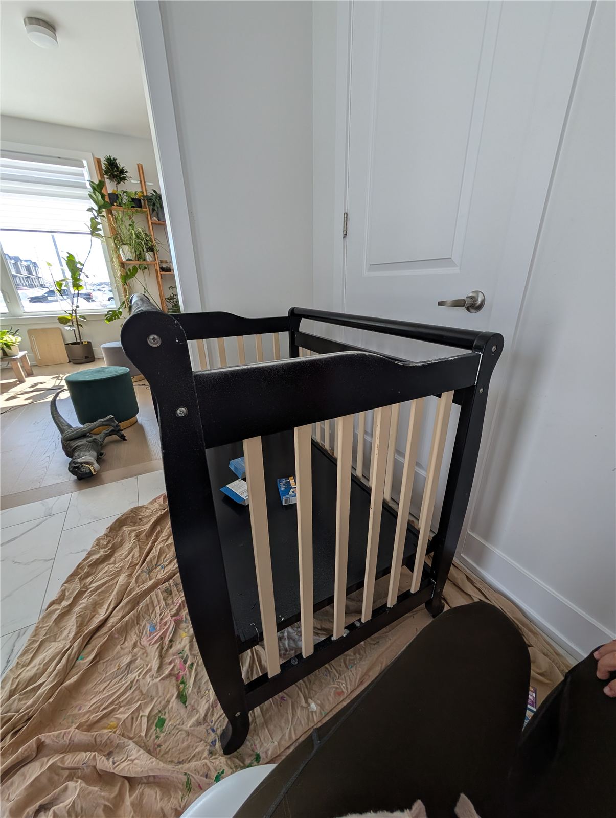 Black mini crib frame sanded down and prepped for repainting, sitting on a drop cloth