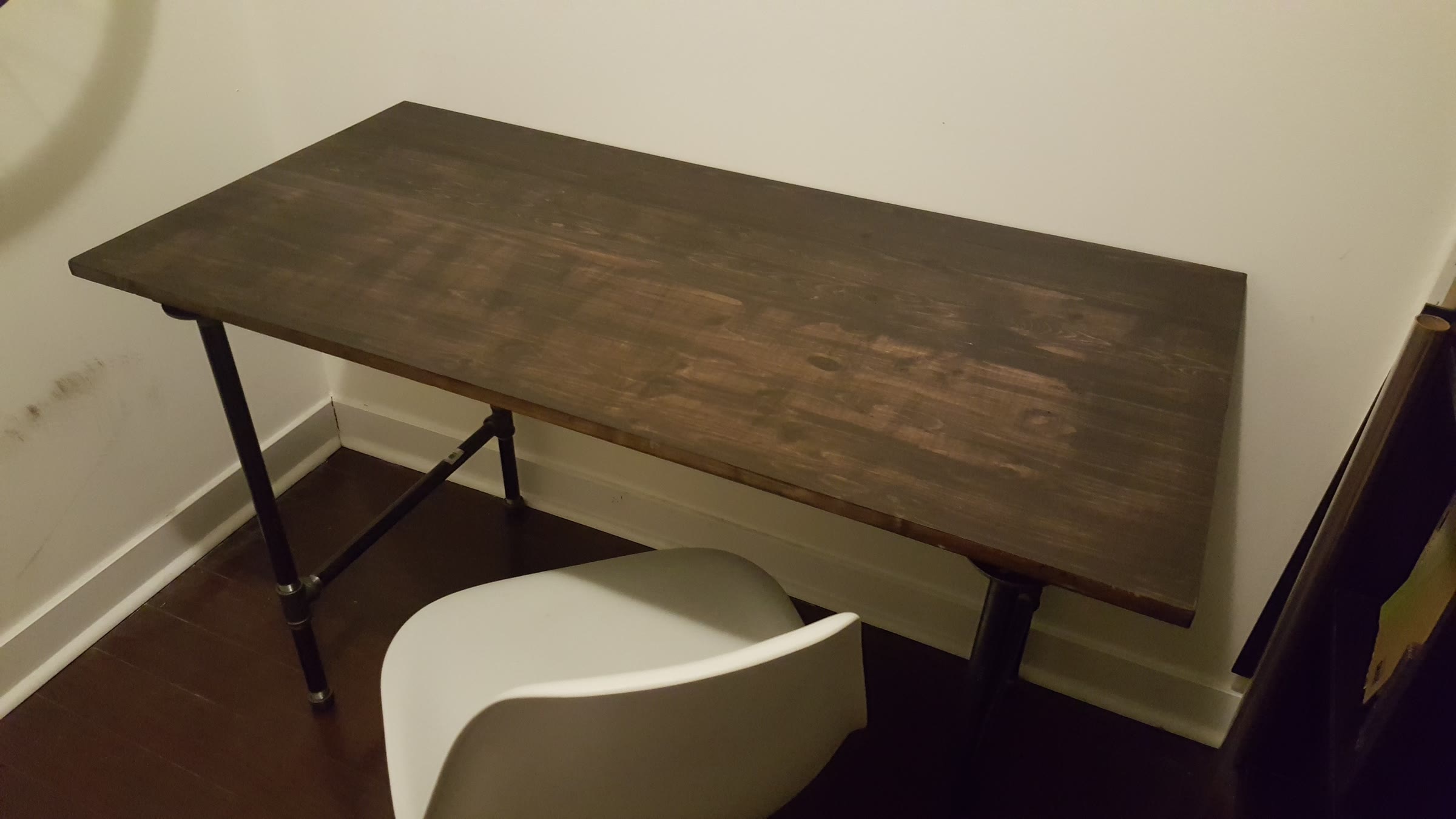 Finished DIY desk with a dark stained wood top and black iron pipe legs with a crossbar, with a white chair