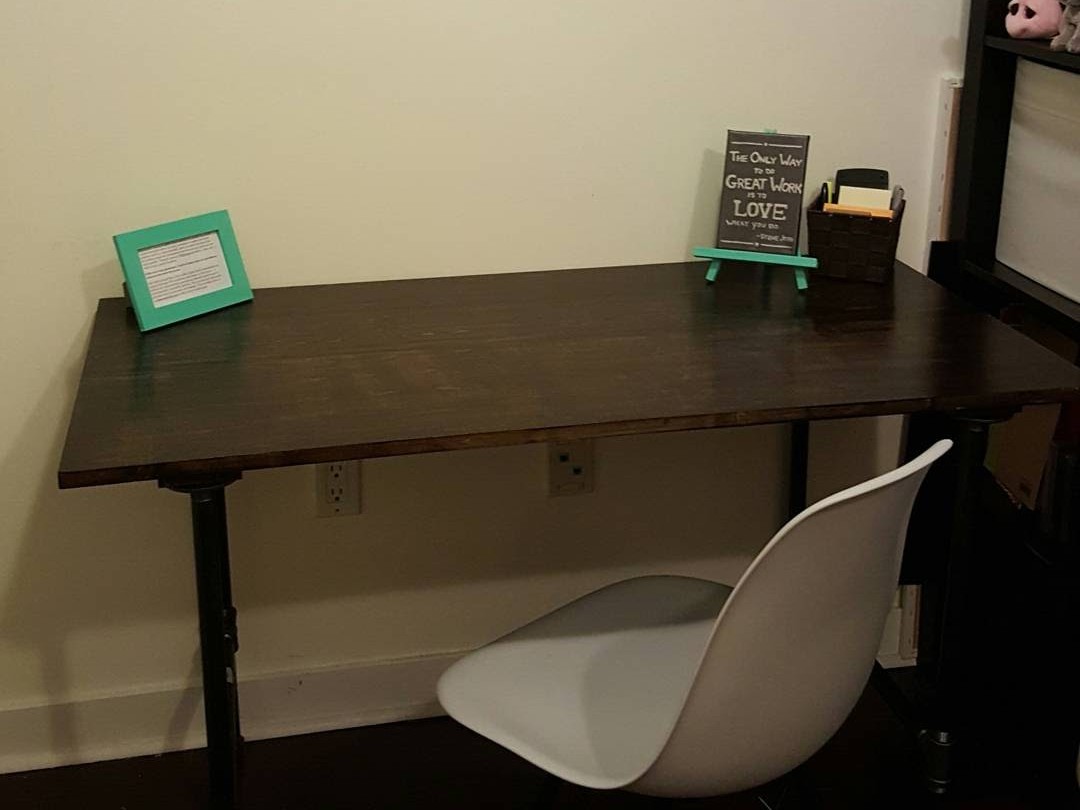 Finished DIY desk with a dark stained wood top and black iron pipe legs, with a teal frame and a small quote sign on top