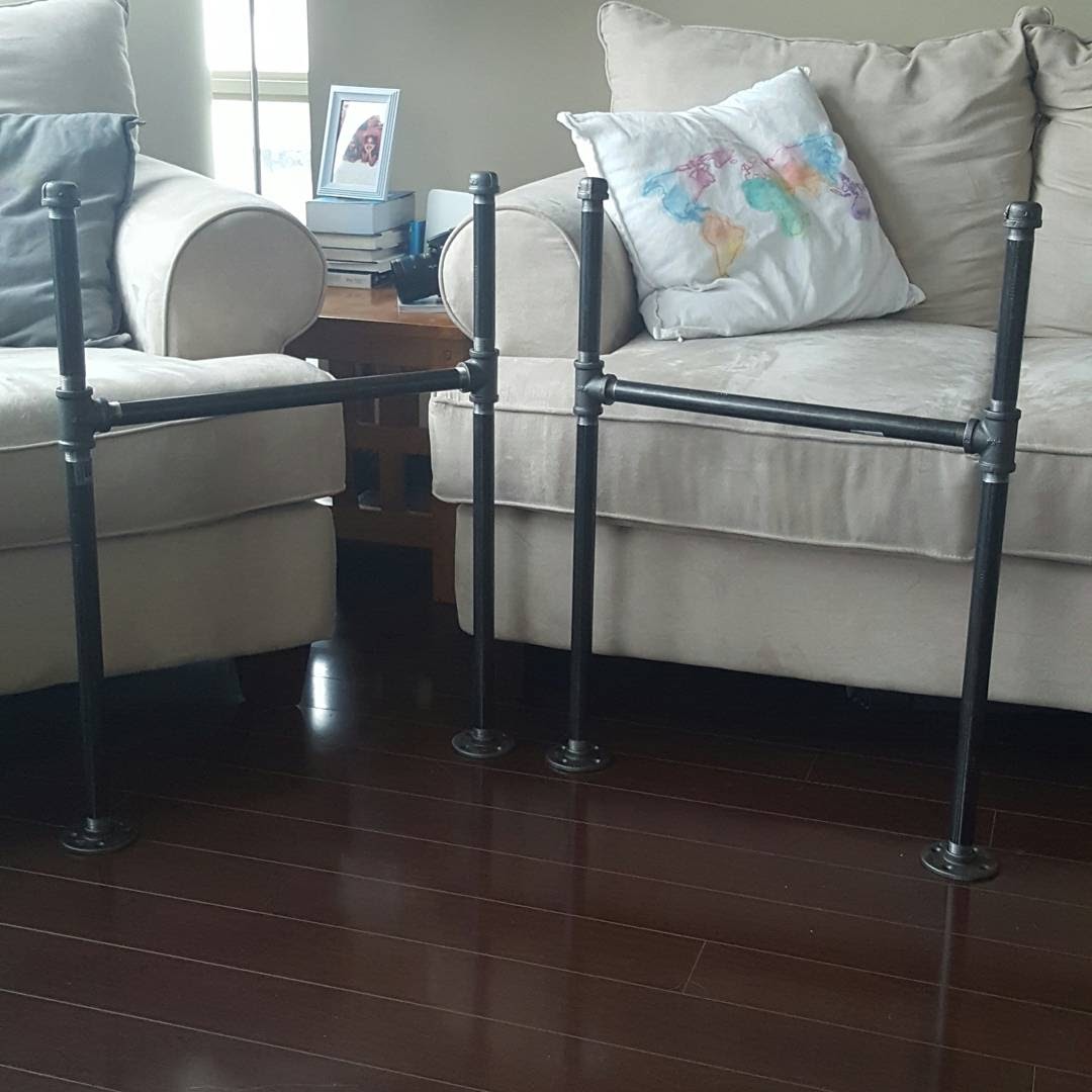 Two assembled black iron pipe leg frames, each with two legs joined by a crossbar, standing on a wood floor