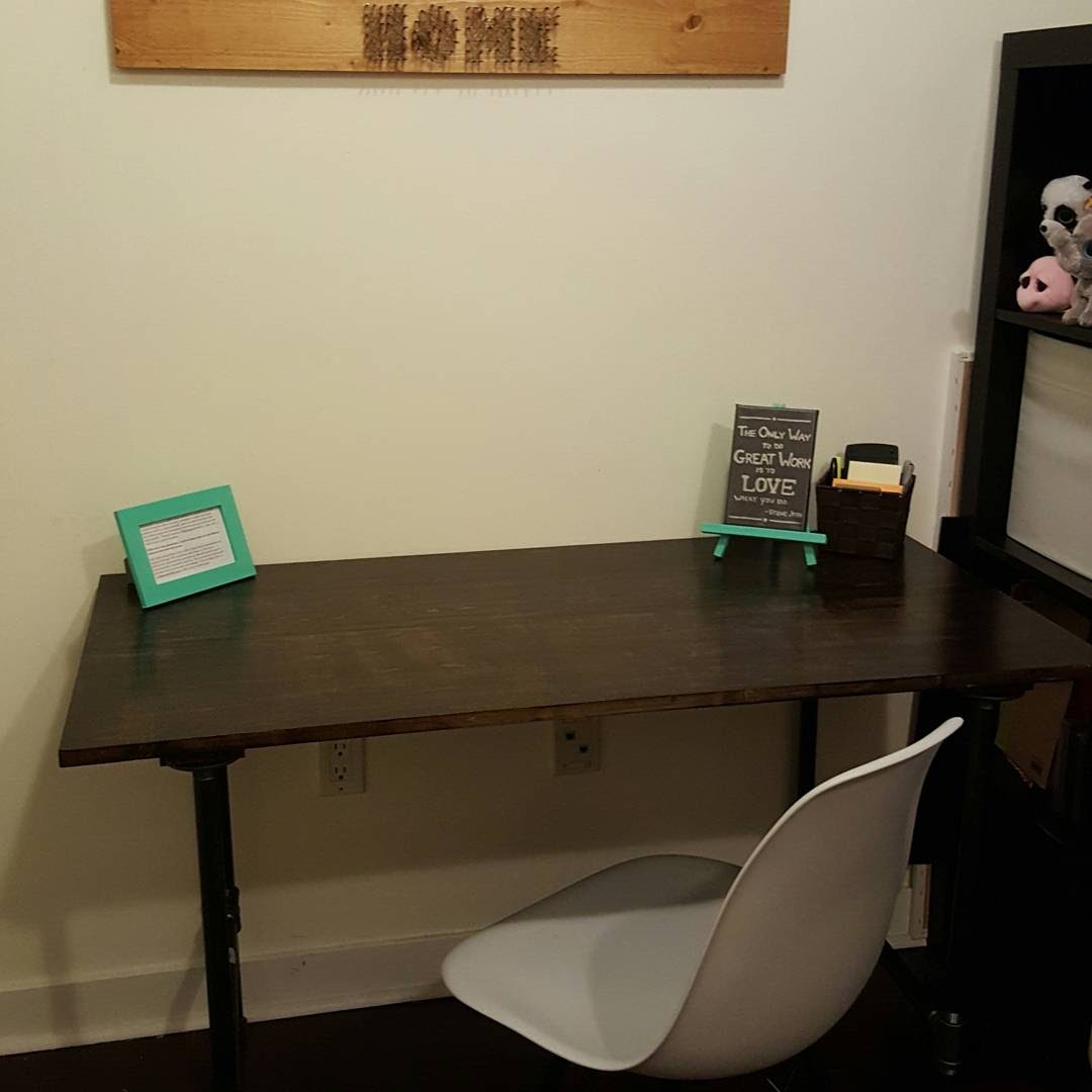 Finished DIY desk with a dark stained wood top and black iron pipe legs, styled with a teal picture frame, a small quote sign, and a desk organizer, with a white chair pulled up
