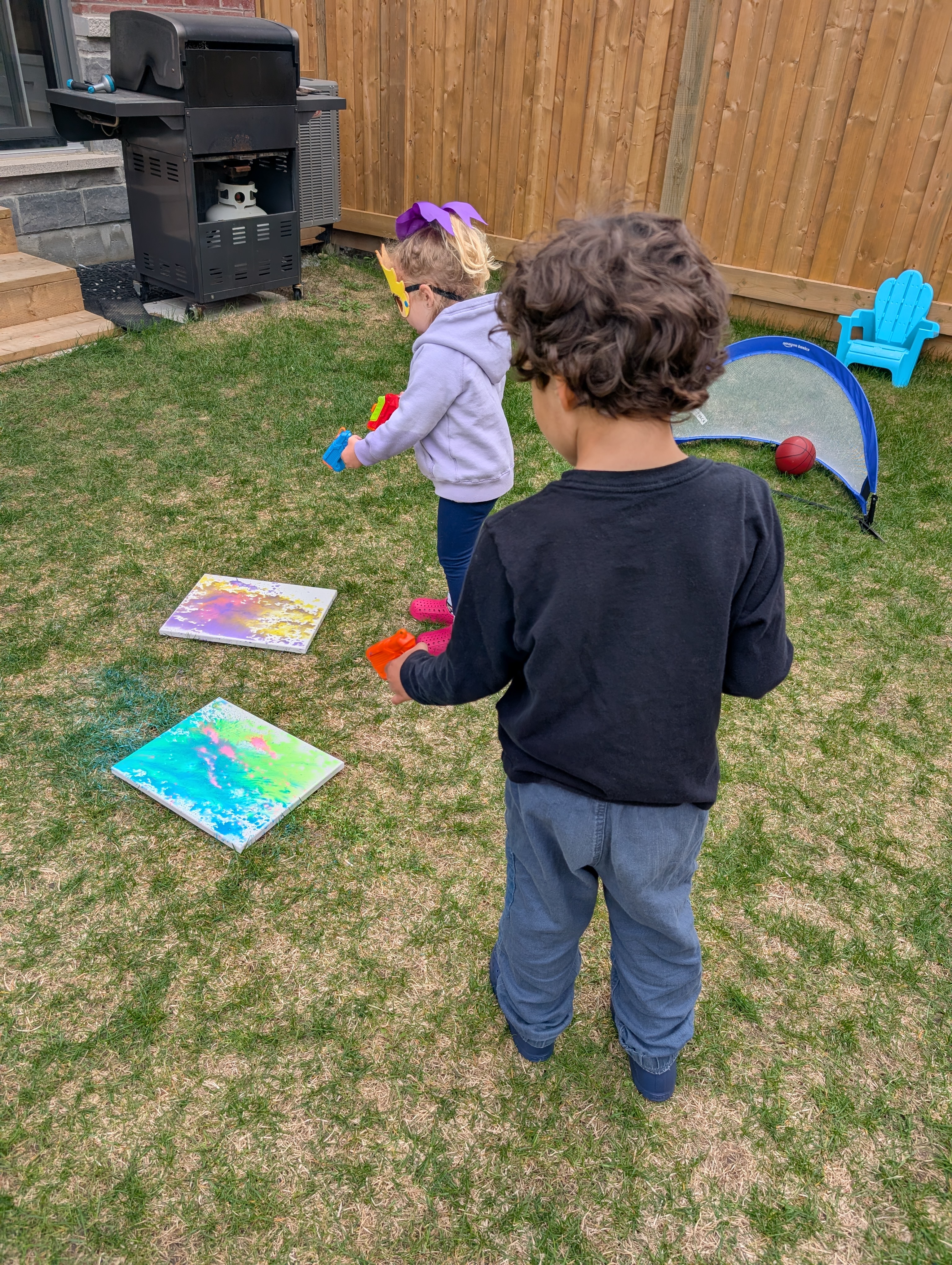 Kids using paint-filled water guns to splatter canvases in the backyard