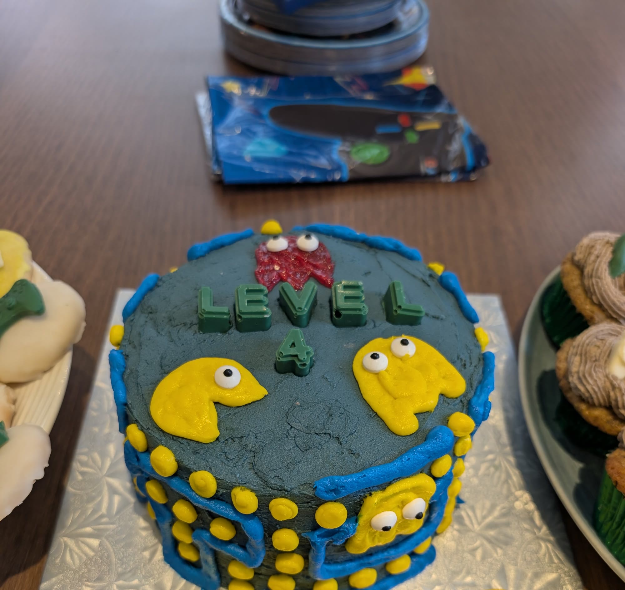 Pac-Man birthday cake decorated with icing only: blue maze lines, yellow dots, two yellow Pac-Man characters, a red ghost, and chocolate letters spelling Level 4
