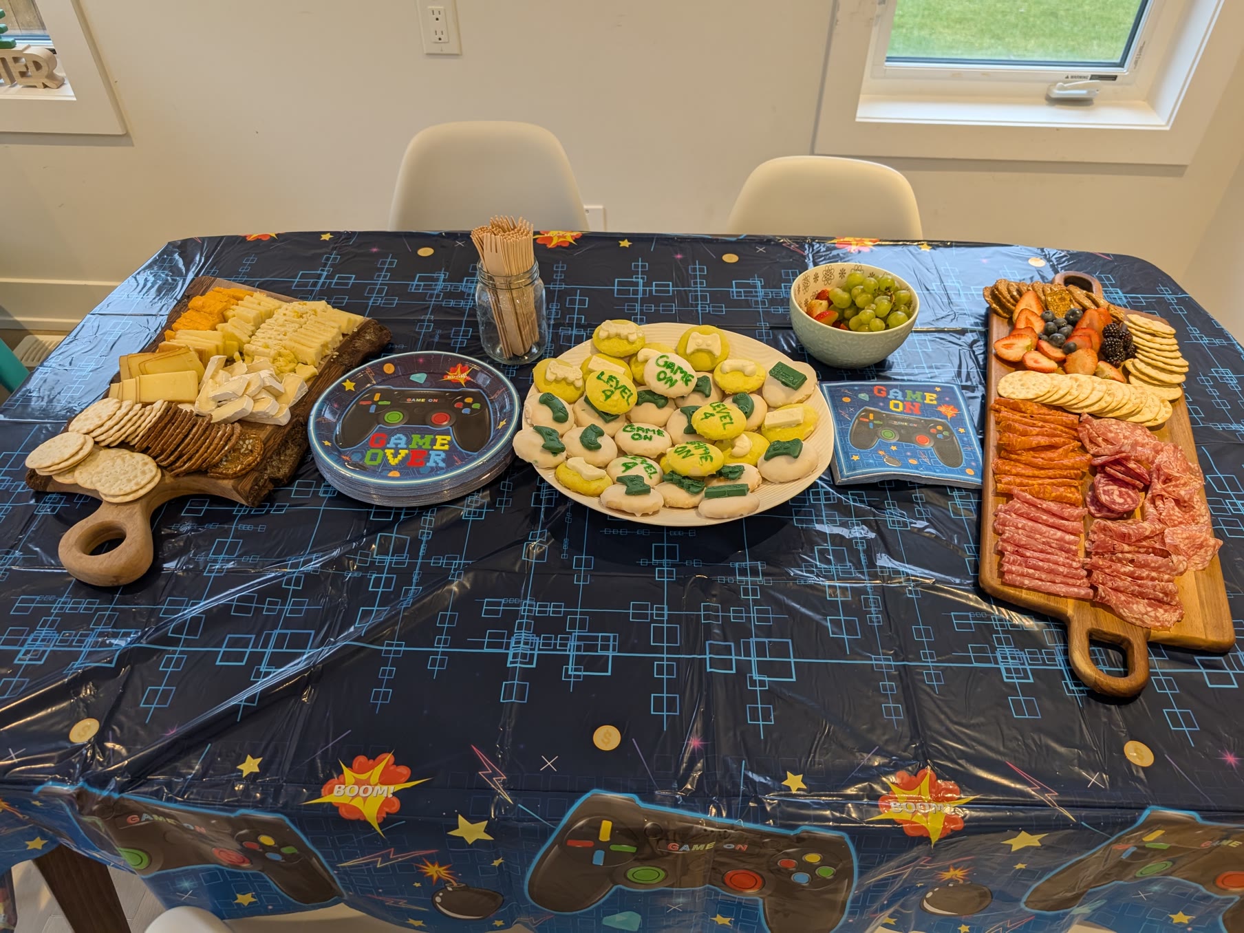 Gamer birthday party table with Game Over plates, Level 4 cookies, and snack boards on a video game controller tablecloth