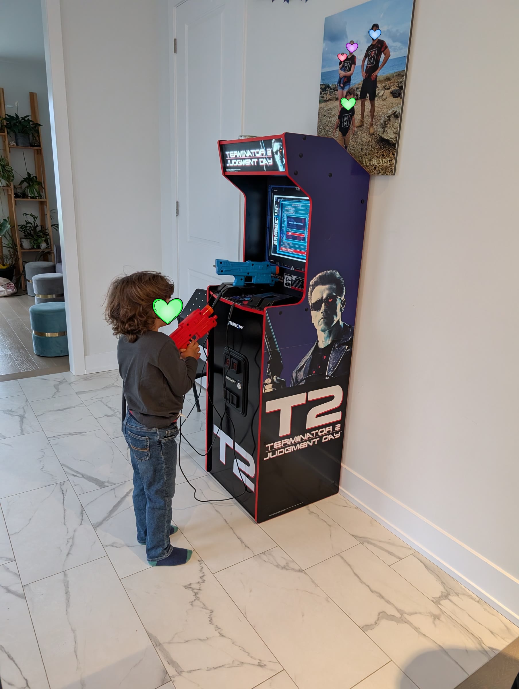 Child playing the Terminator 2 Judgment Day arcade machine with the light gun, with a coloured heart covering the face