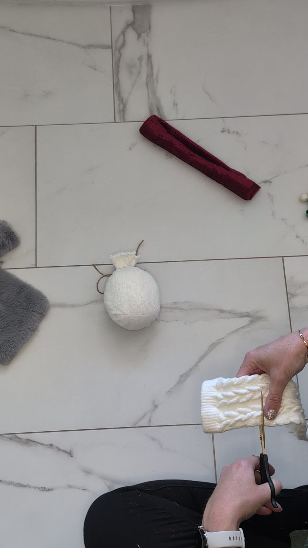 Cutting a cream cable-knit sock with scissors while a stuffed, tied sock sits on the floor