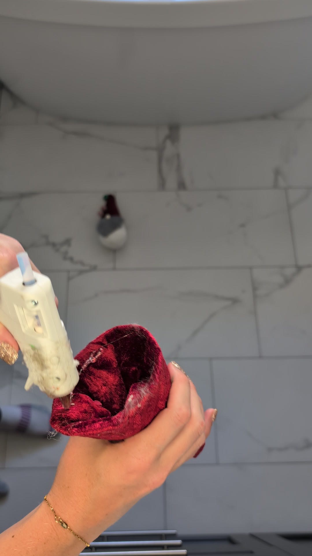 Gluing the red velvet hat onto the sock gnome with the wood bead nose and grey faux fur beard