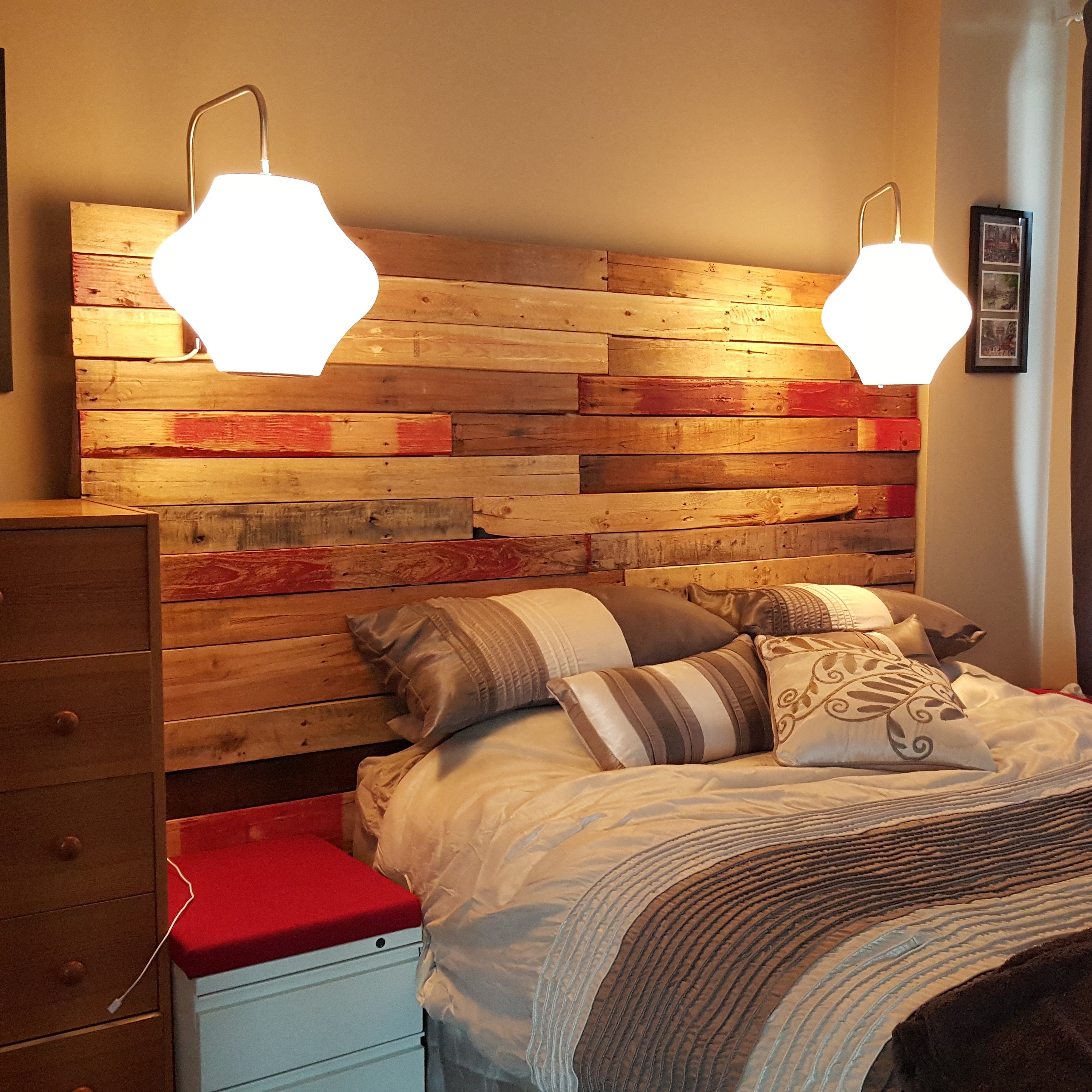 Finished reclaimed skid wood headboard mounted on the wall with two glowing pendant sconces above a made bed