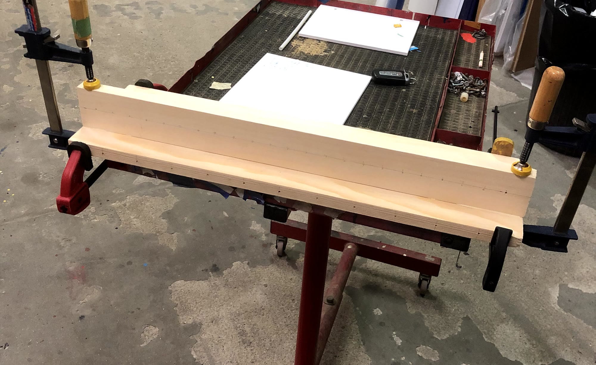 Three pine boards glued and clamped together to form a back panel and a ledge, with a row of small pilot holes marked along the seam