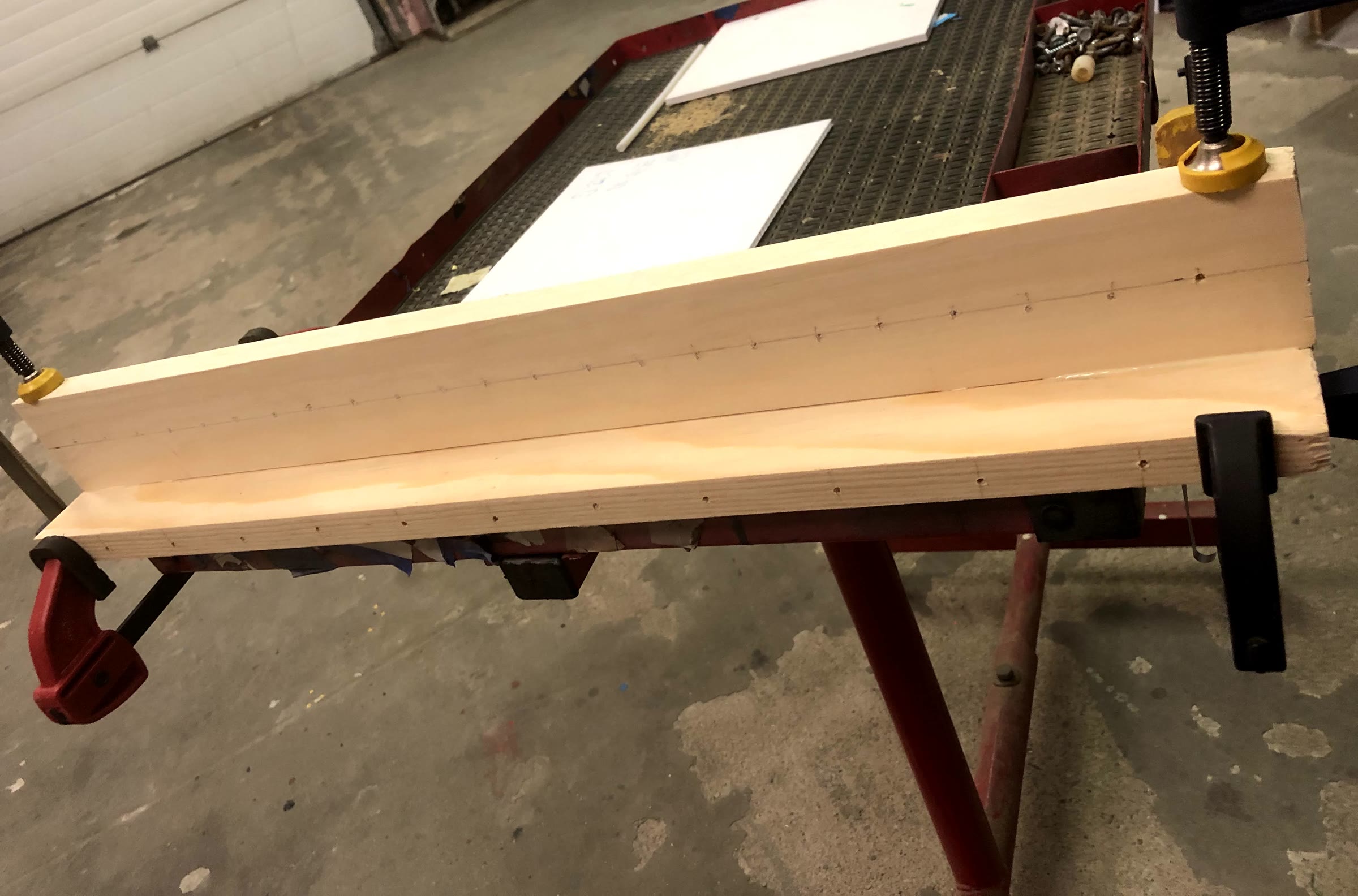 Side view of the clamped boards showing the evenly spaced pilot holes along the ledge and the back panel