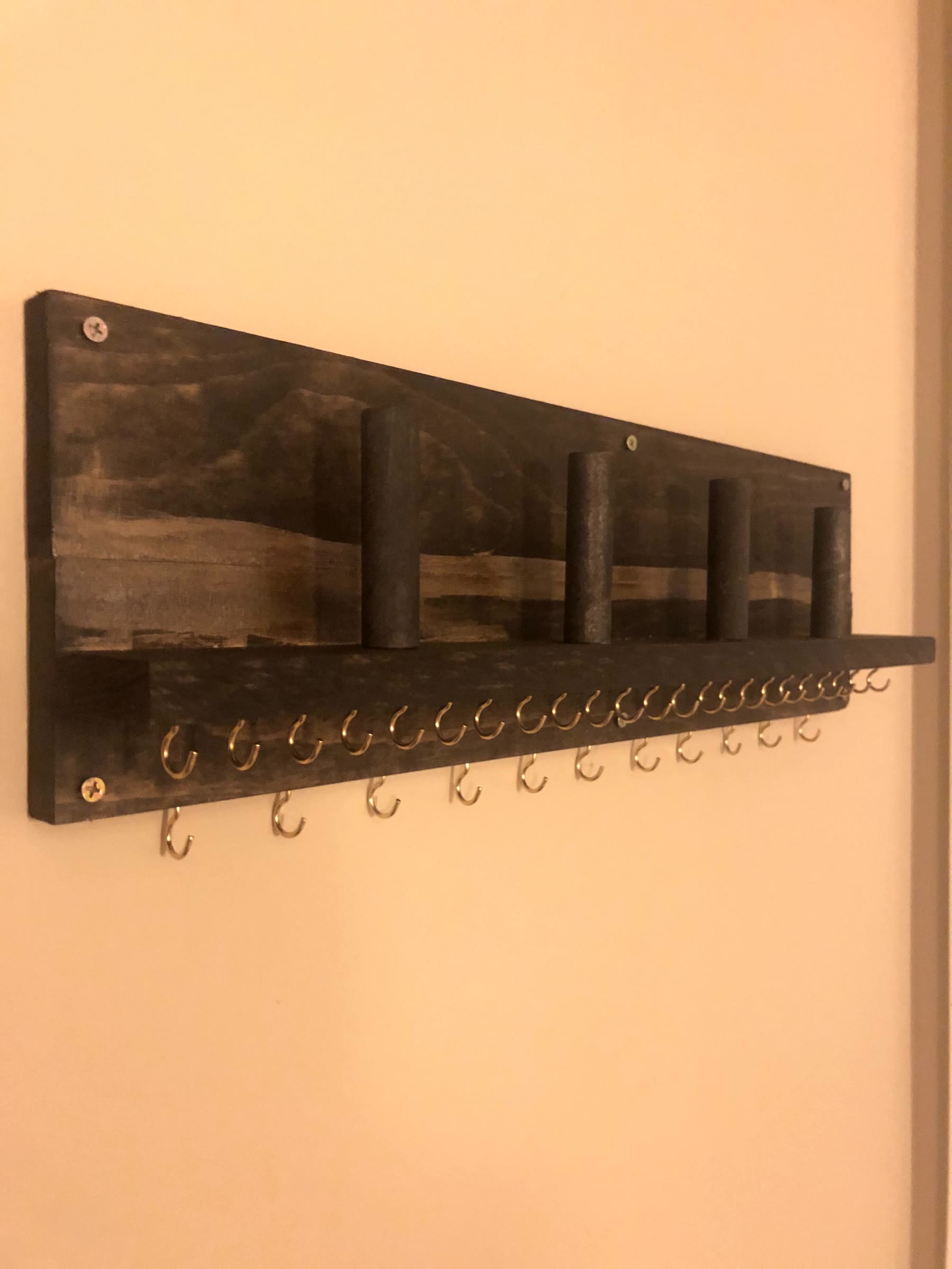 Side angle of the finished dark stained jewelry holder before use, with two staggered rows of brass hooks, a ledge, and four upright dowels