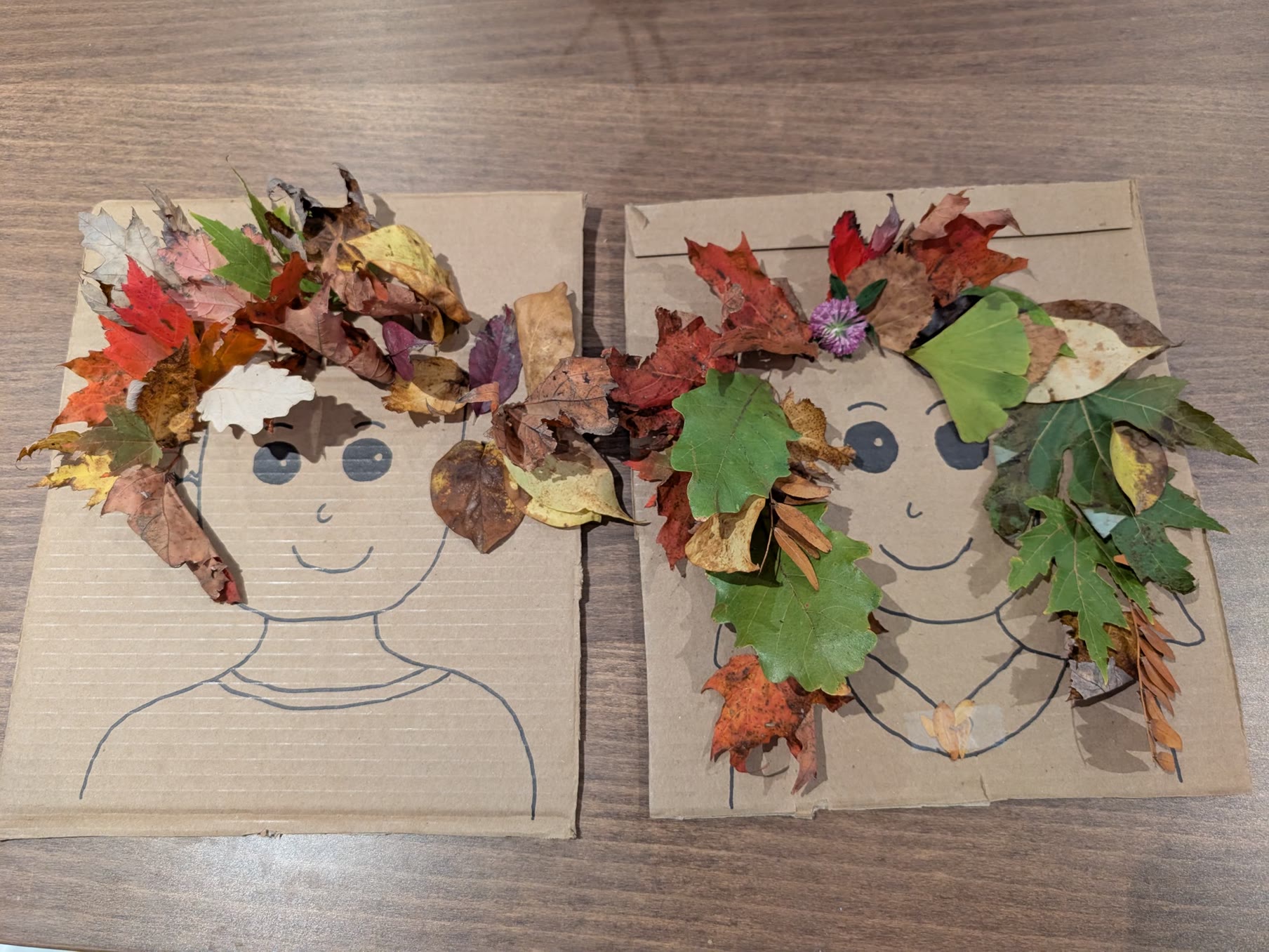 Two cardboard faces with hair made from colorful fall leaves