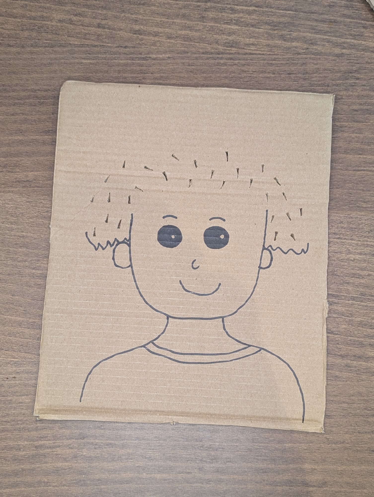 Cardboard face drawn with a marker, with small slits cut into the top and sides where the hair goes