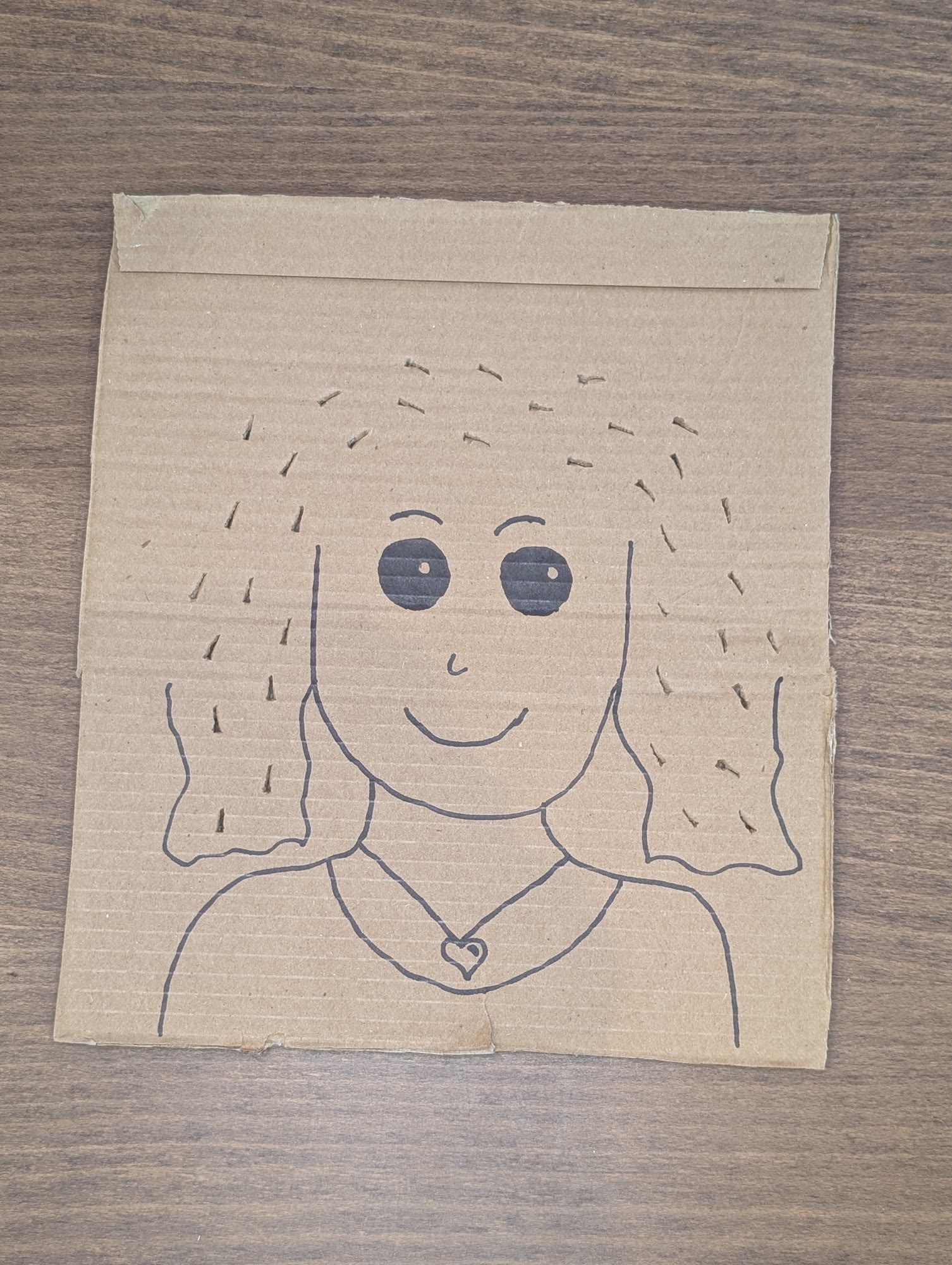Cardboard face with long hair outlined in marker and small slits cut along the hair