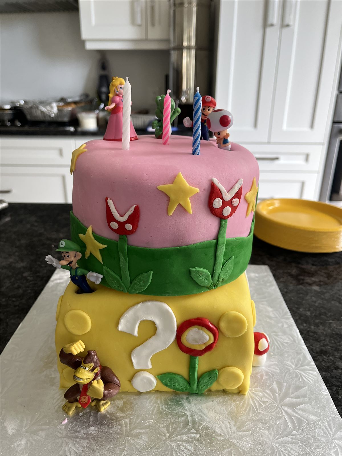 Two-tier Super Mario themed birthday cake with character figures and candles