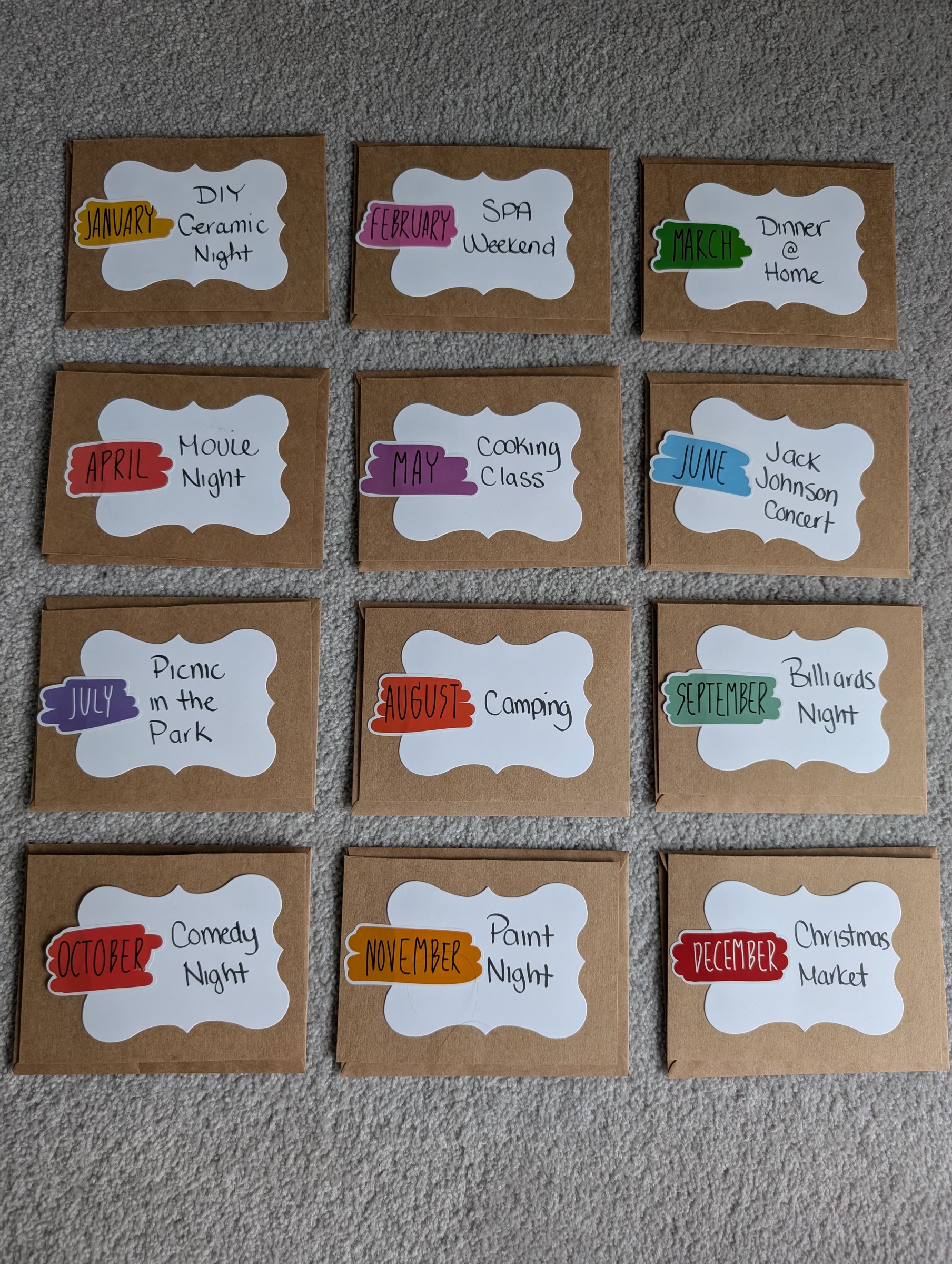 Twelve kraft cards, each with a white ornate tag, a coloured month sticker, and a handwritten date such as DIY Ceramic Night, Spa Weekend, and Christmas Market