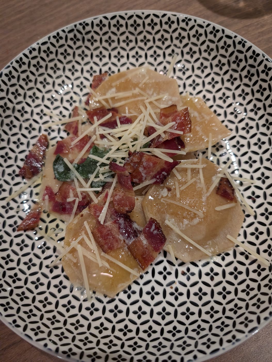 Homemade butternut squash ravioli topped with crispy bacon, sage, and shredded cheese in a patterned bowl
