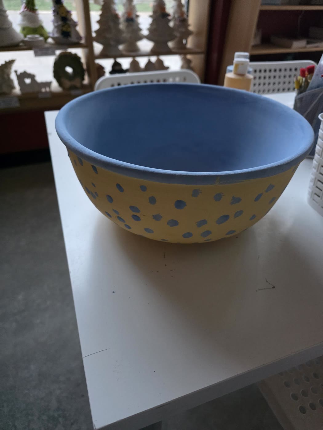 A hand-painted ceramic bowl, yellow with blue dots on the outside and solid blue on the inside