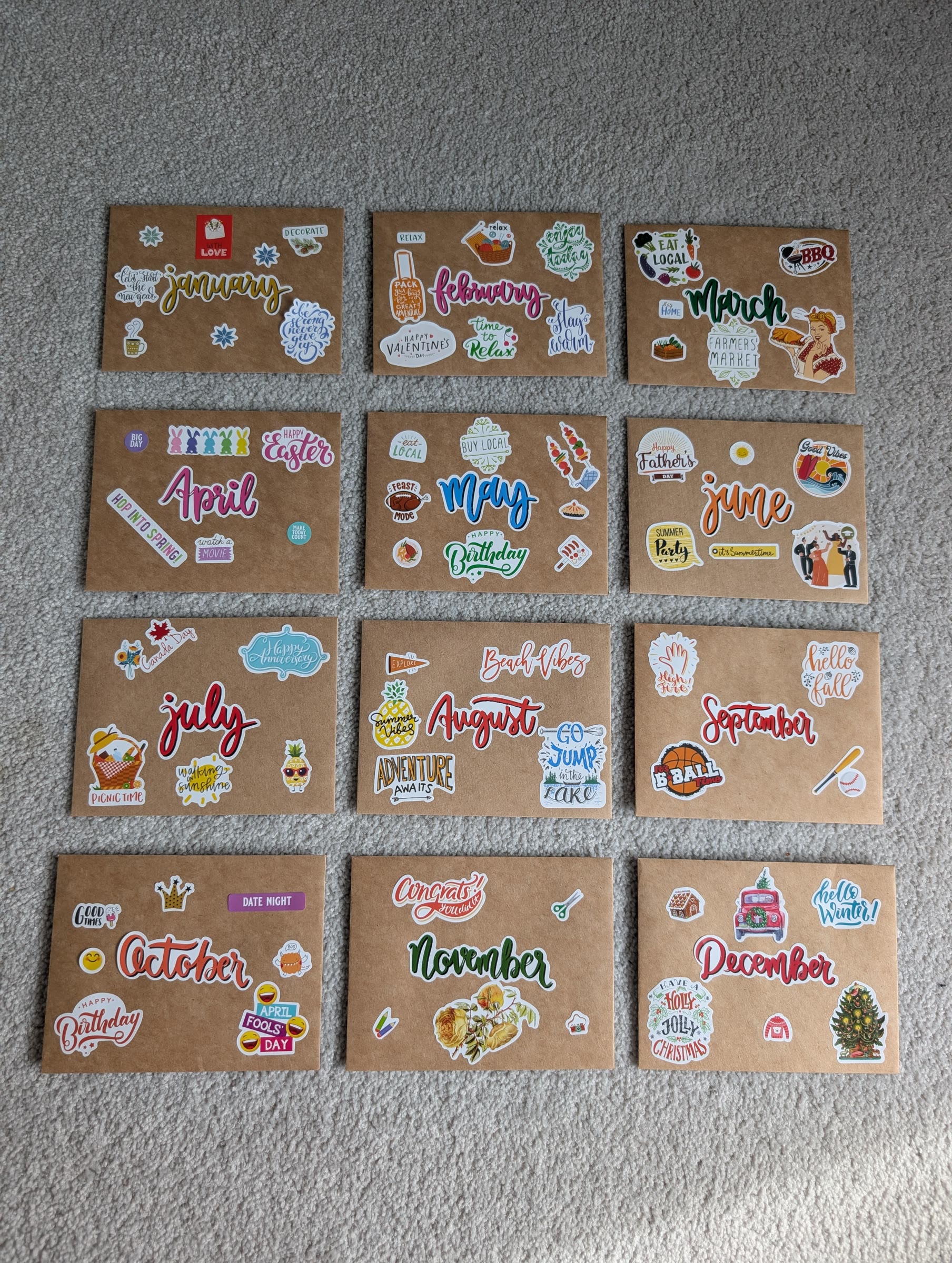 Twelve kraft envelopes laid out in a grid, one for each month from January to December, each covered in stickers that hint at that month's date
