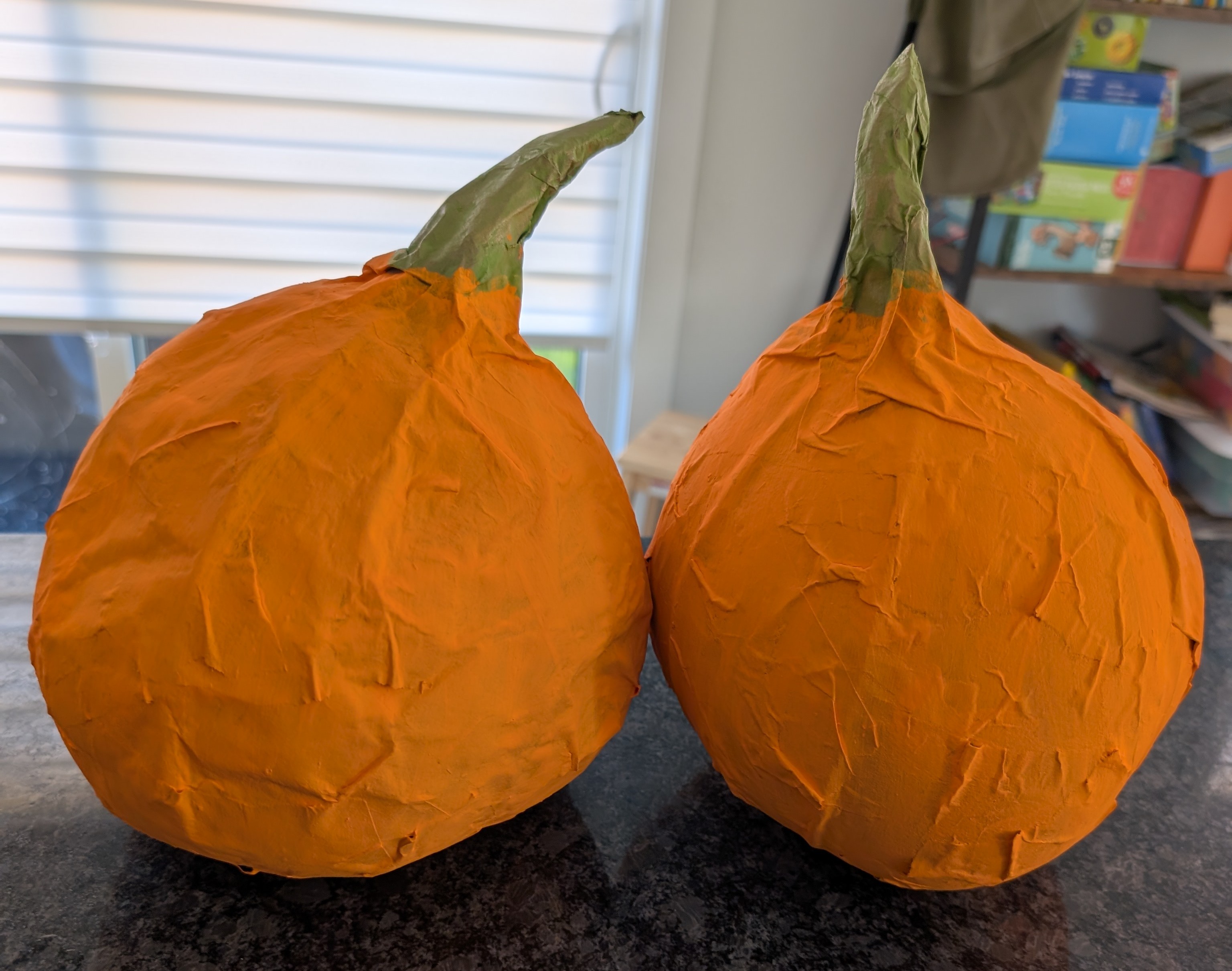 Two finished paper mache pumpkins painted orange with green stems