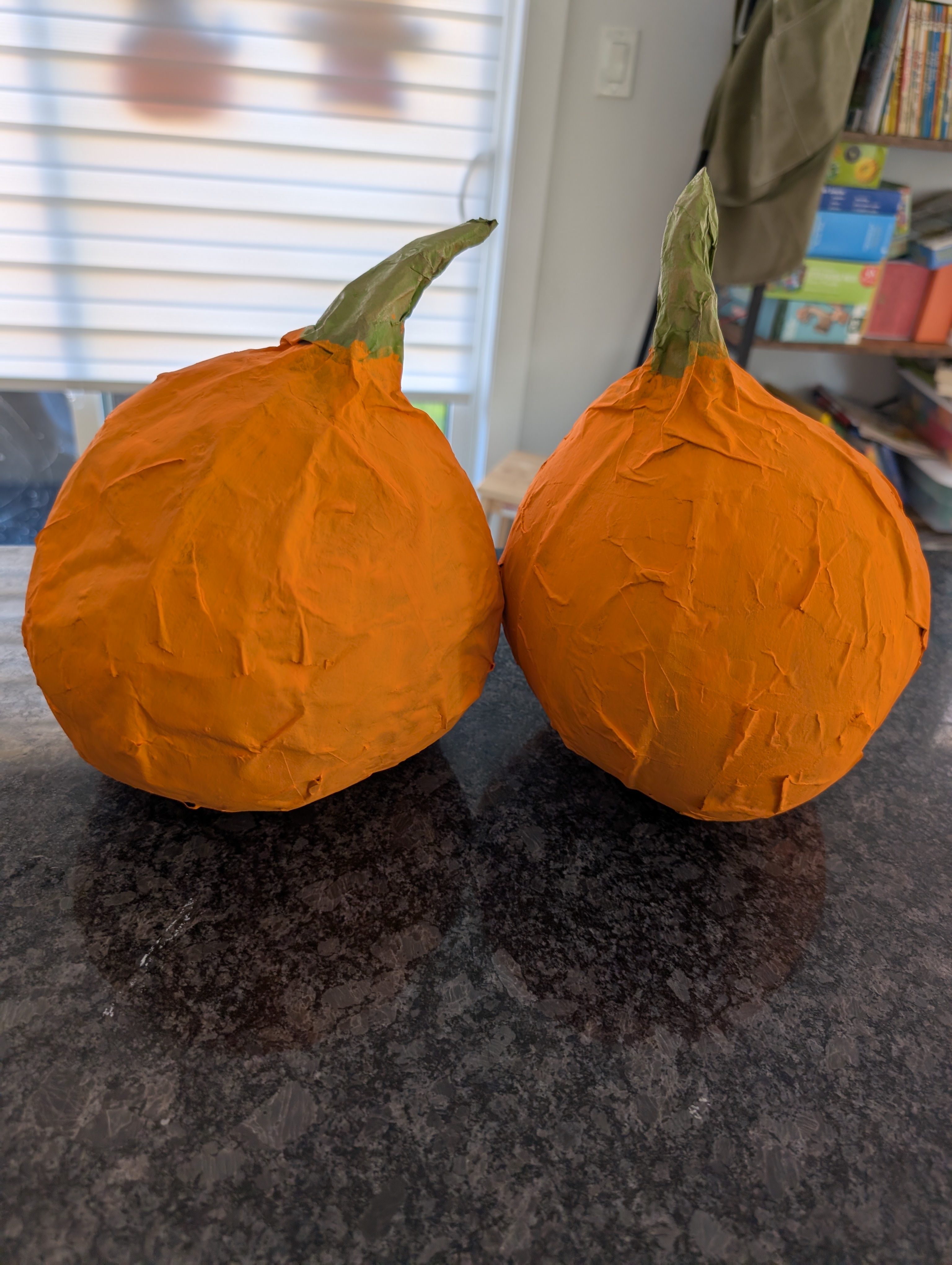 Two finished paper mache pumpkins painted orange with green stems