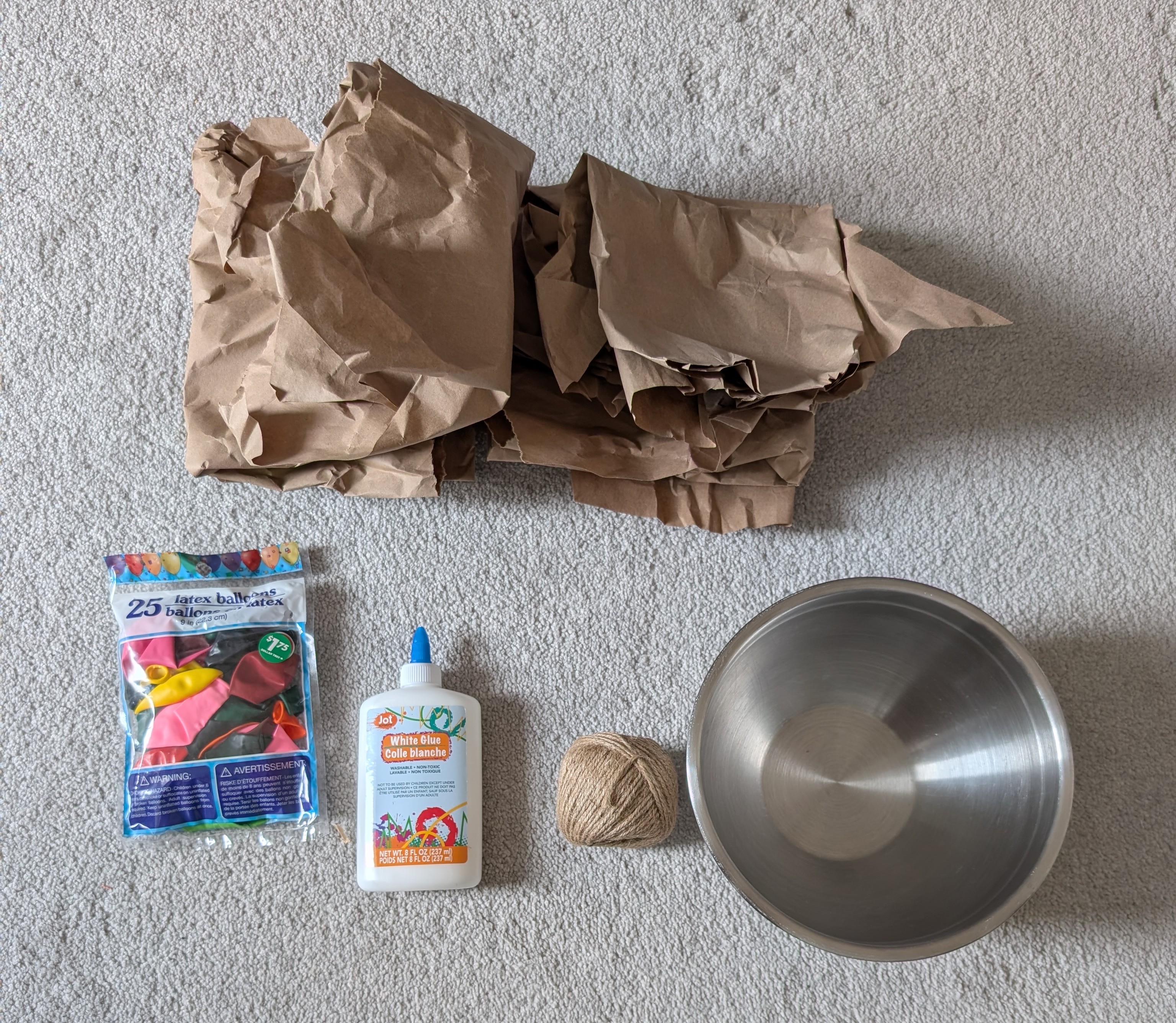 Materials laid out: craft paper, a mixing bowl, twine, white glue, and a pack of balloons