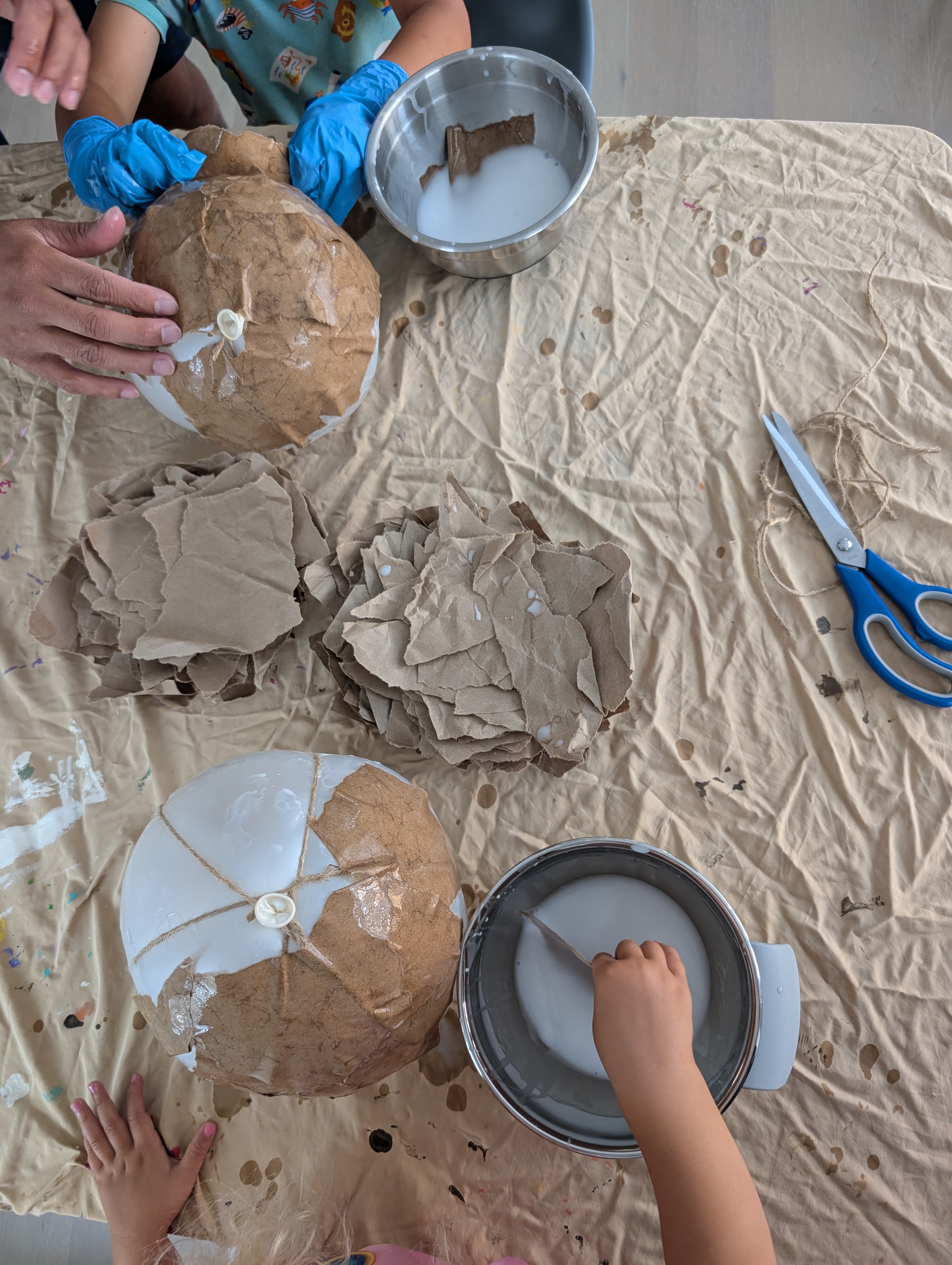 Hands layering glue-soaked craft paper strips over a rope-wrapped balloon