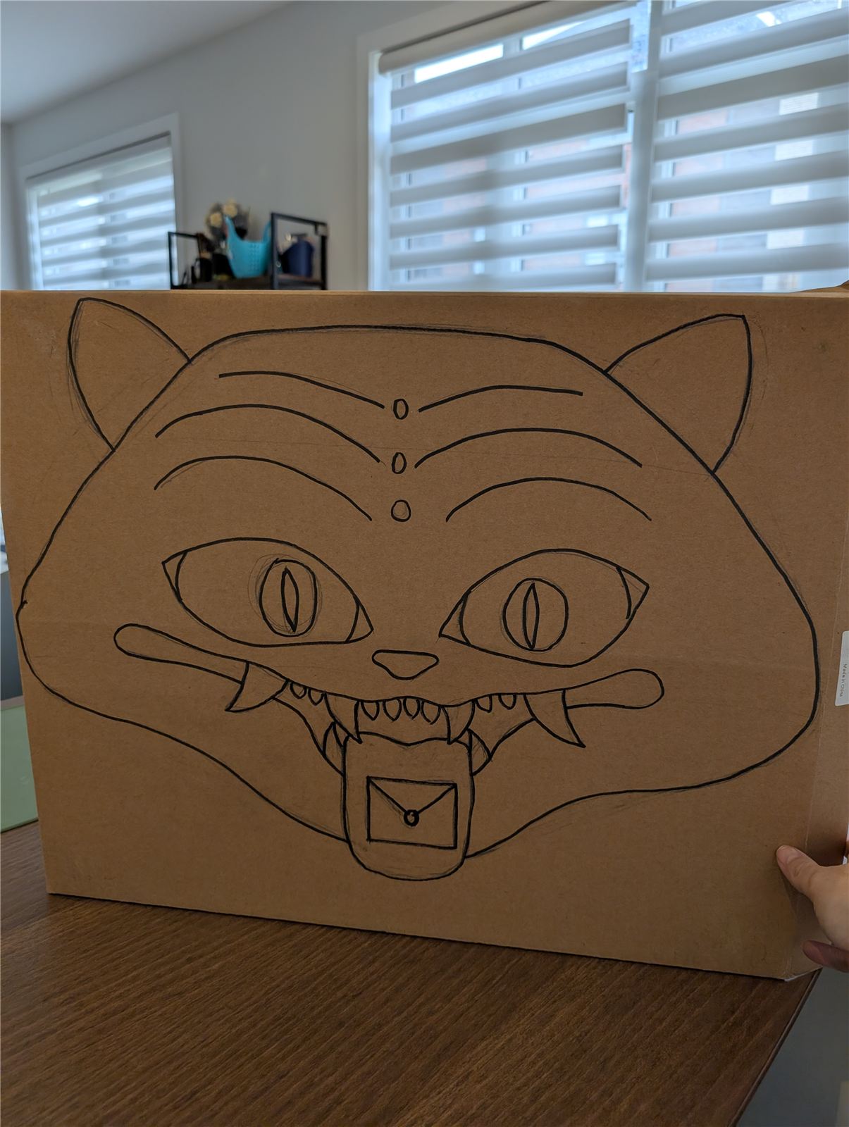 Demon cat face sketched in pen on a cardboard box for the pinata