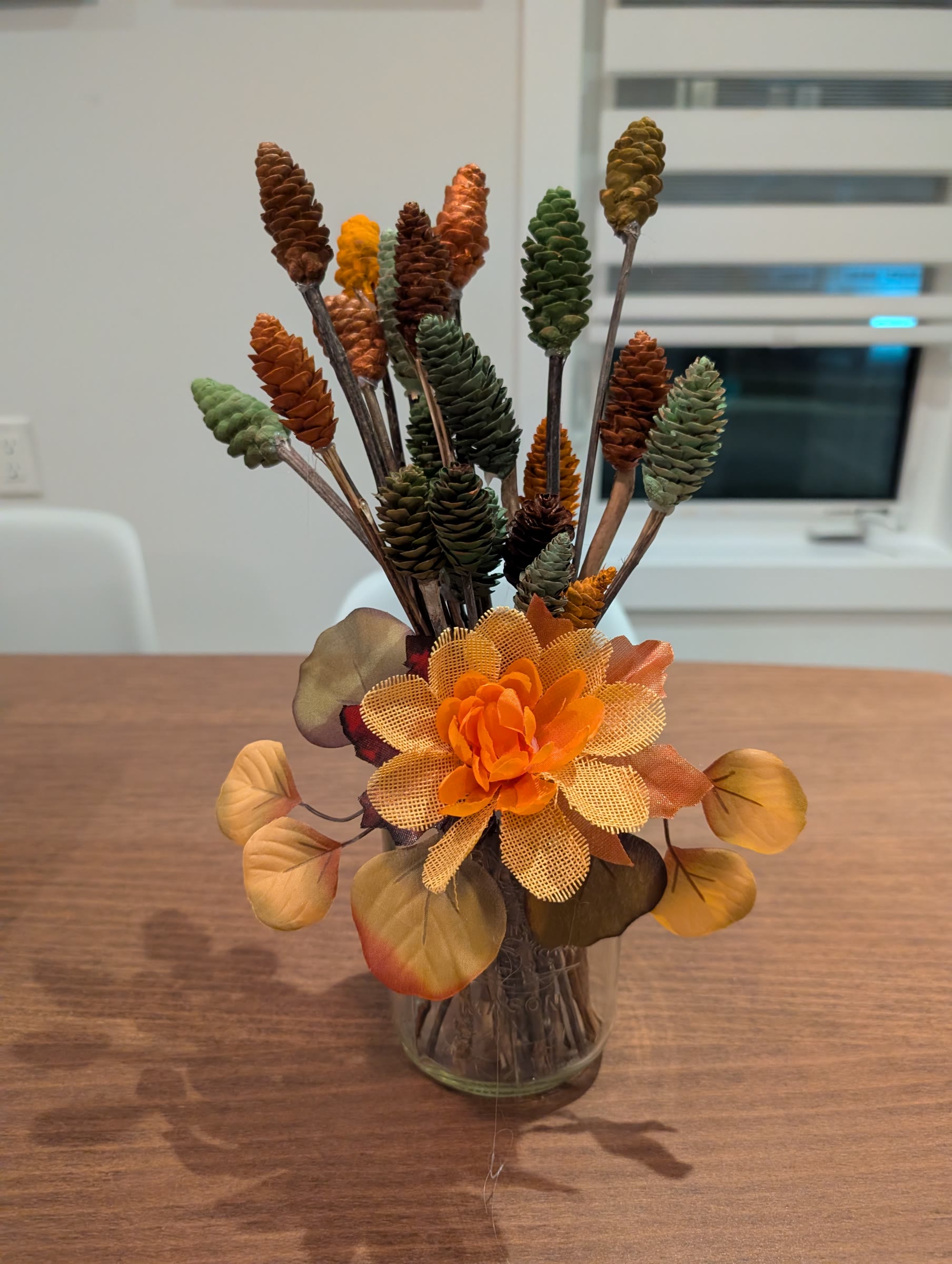 Bouquet of painted pinecones on sticks in a glass mason jar, finished with a burlap flower and fall leaves