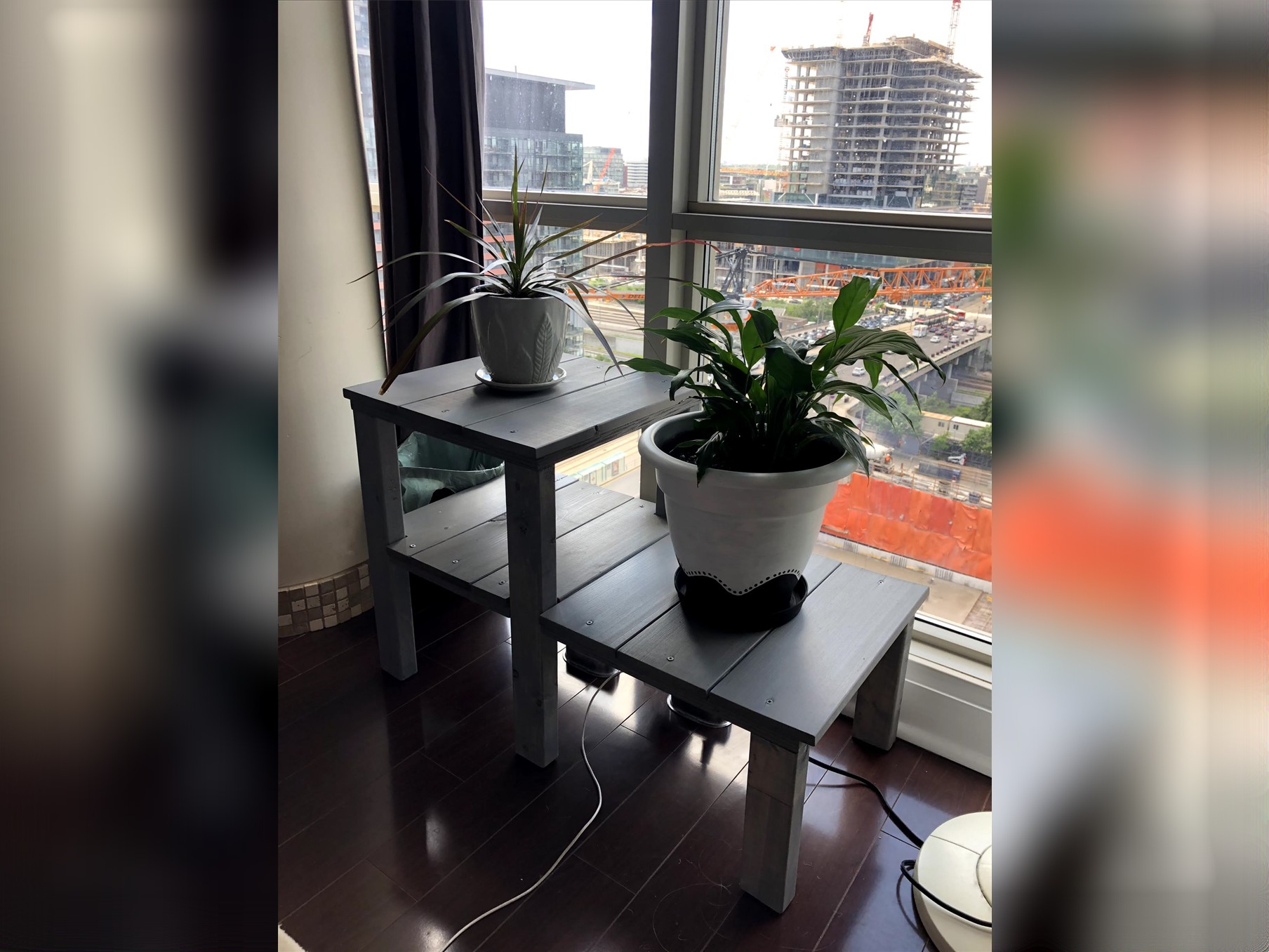 Finished weathered grey two-level plant stand holding two potted plants by a window