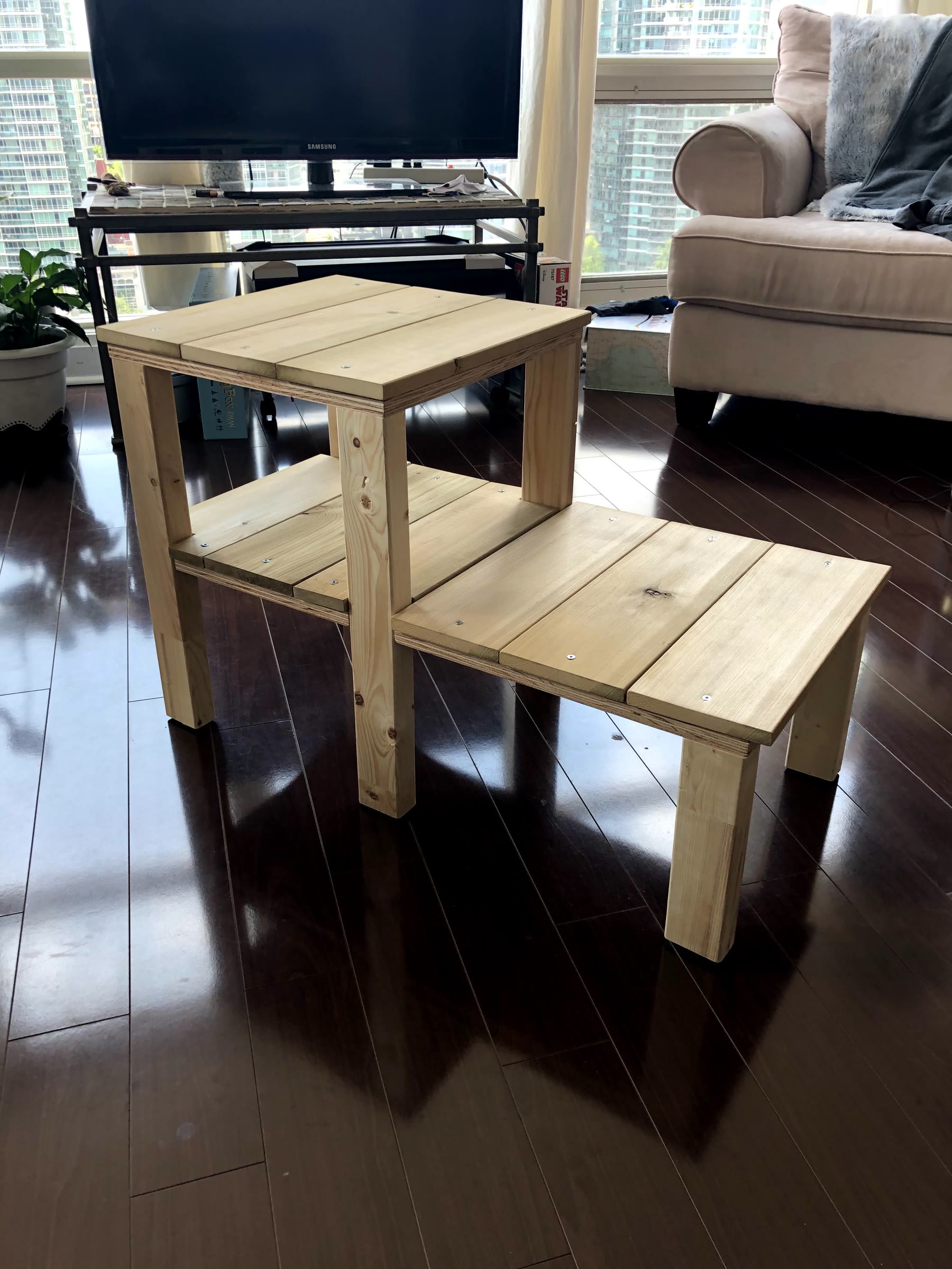 Front view of the assembled unstained plant stand on a hardwood floor, with the plywood edge visible under each platform