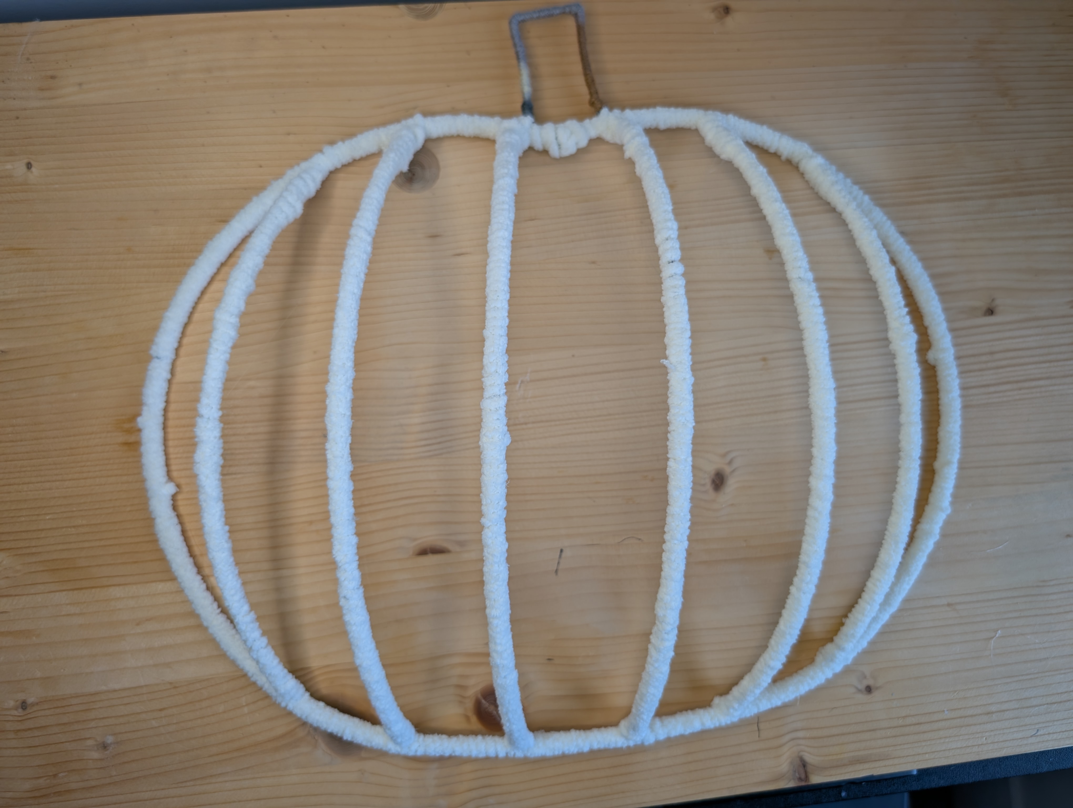 Wire pumpkin frame fully wrapped in cream yarn, laid flat on a wood surface