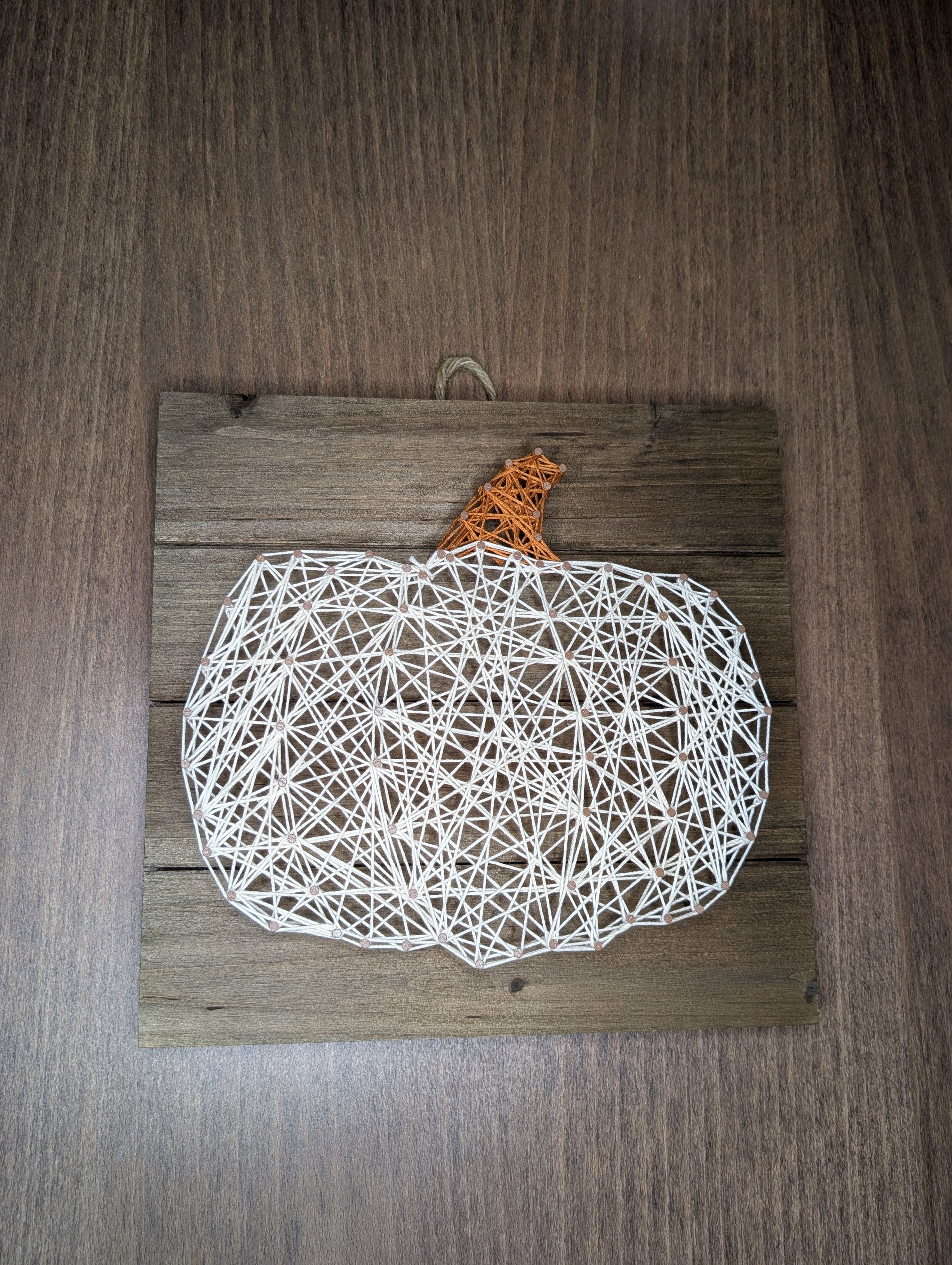 Finished pumpkin string art in white and orange thread on a stained wood plank board