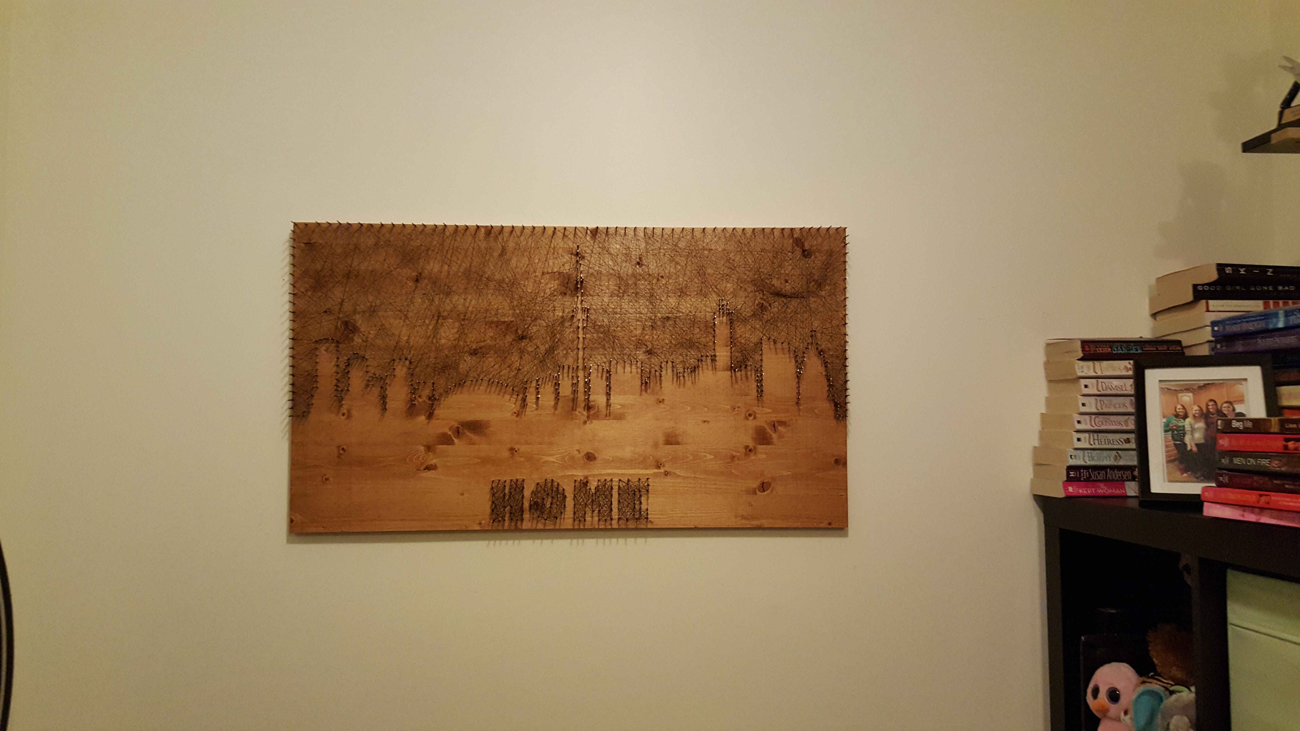 Large string art on a stained wood board hanging on a wall, with a city skyline above the word HOME