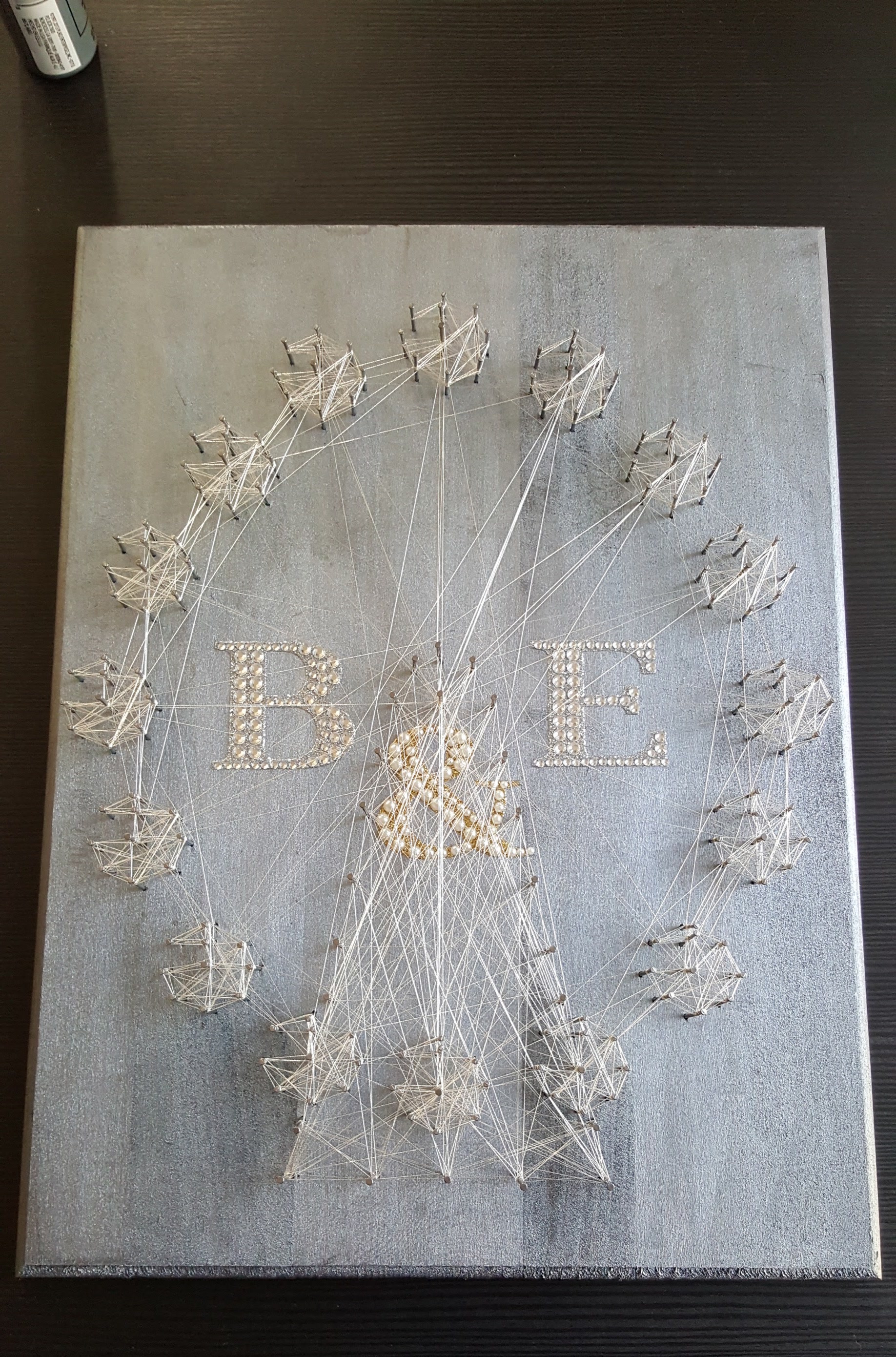 B and E monogram string art with a Ferris wheel in white thread and rhinestone letters on a silver board