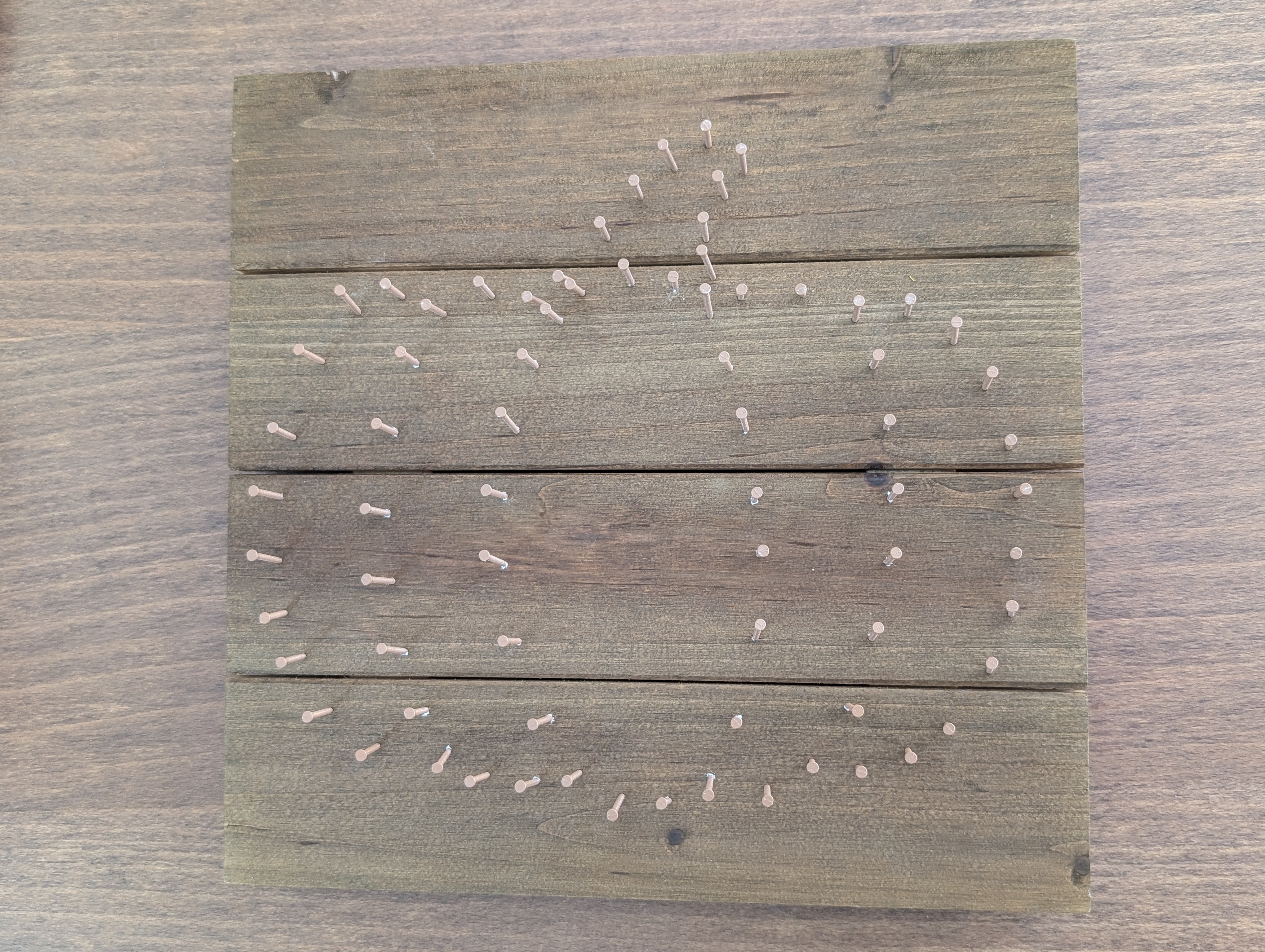 Nails hammered around the outline of a pumpkin shape on stained wood