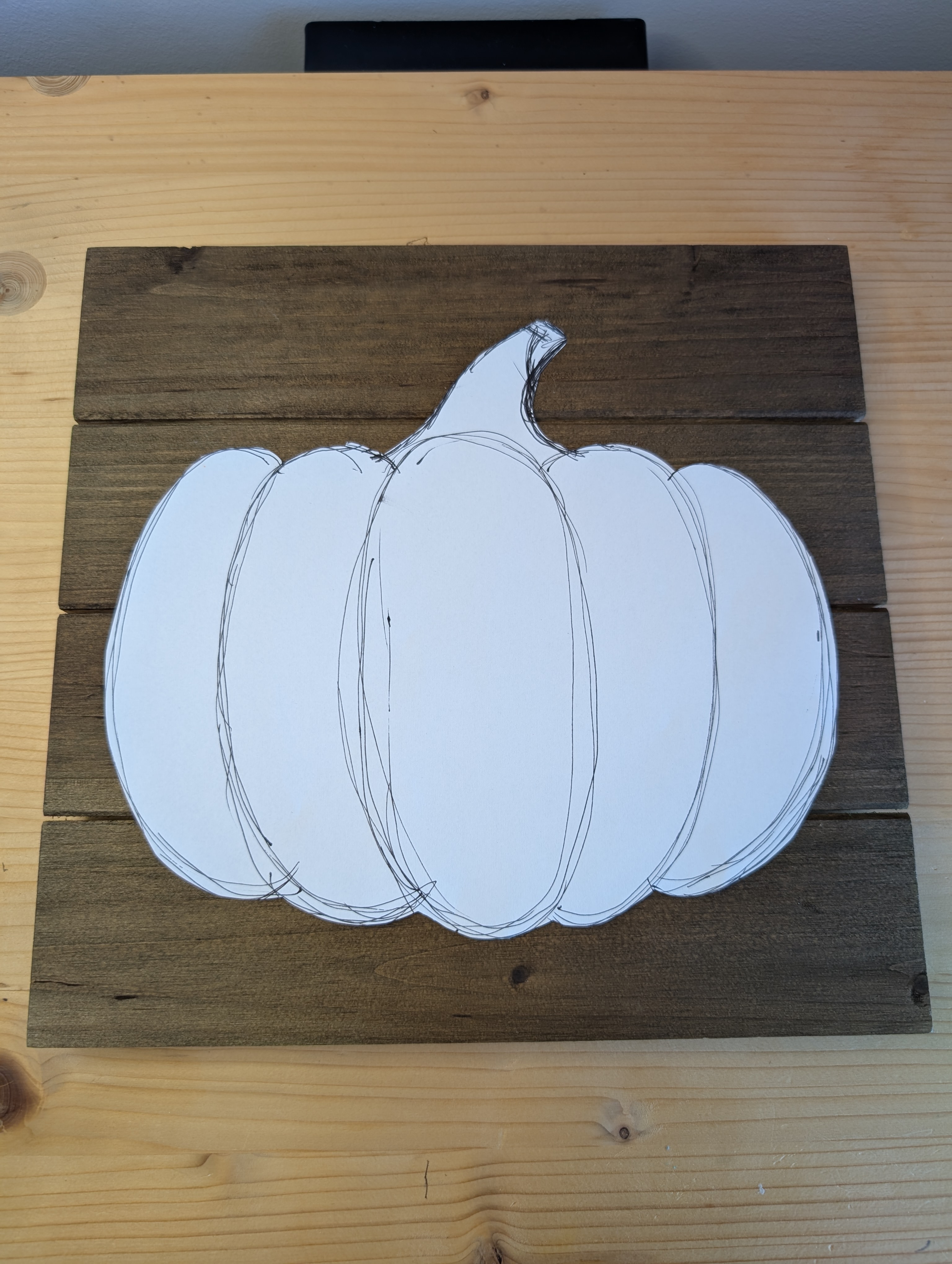 Paper pumpkin template traced onto a stained wood plank board