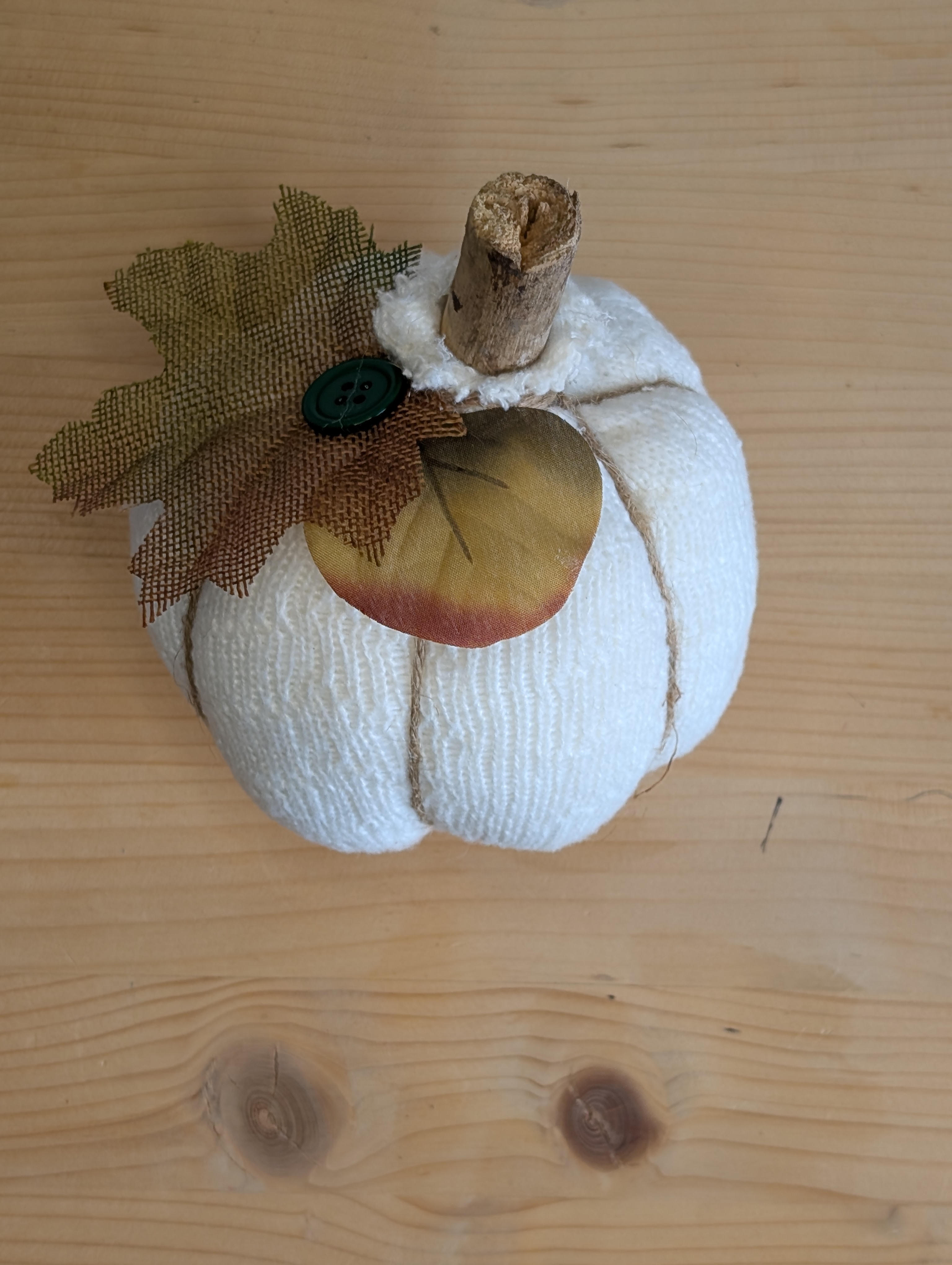 Finished sock pumpkin on a wood table with a stick stem, twine ridges, burlap leaf, and green button