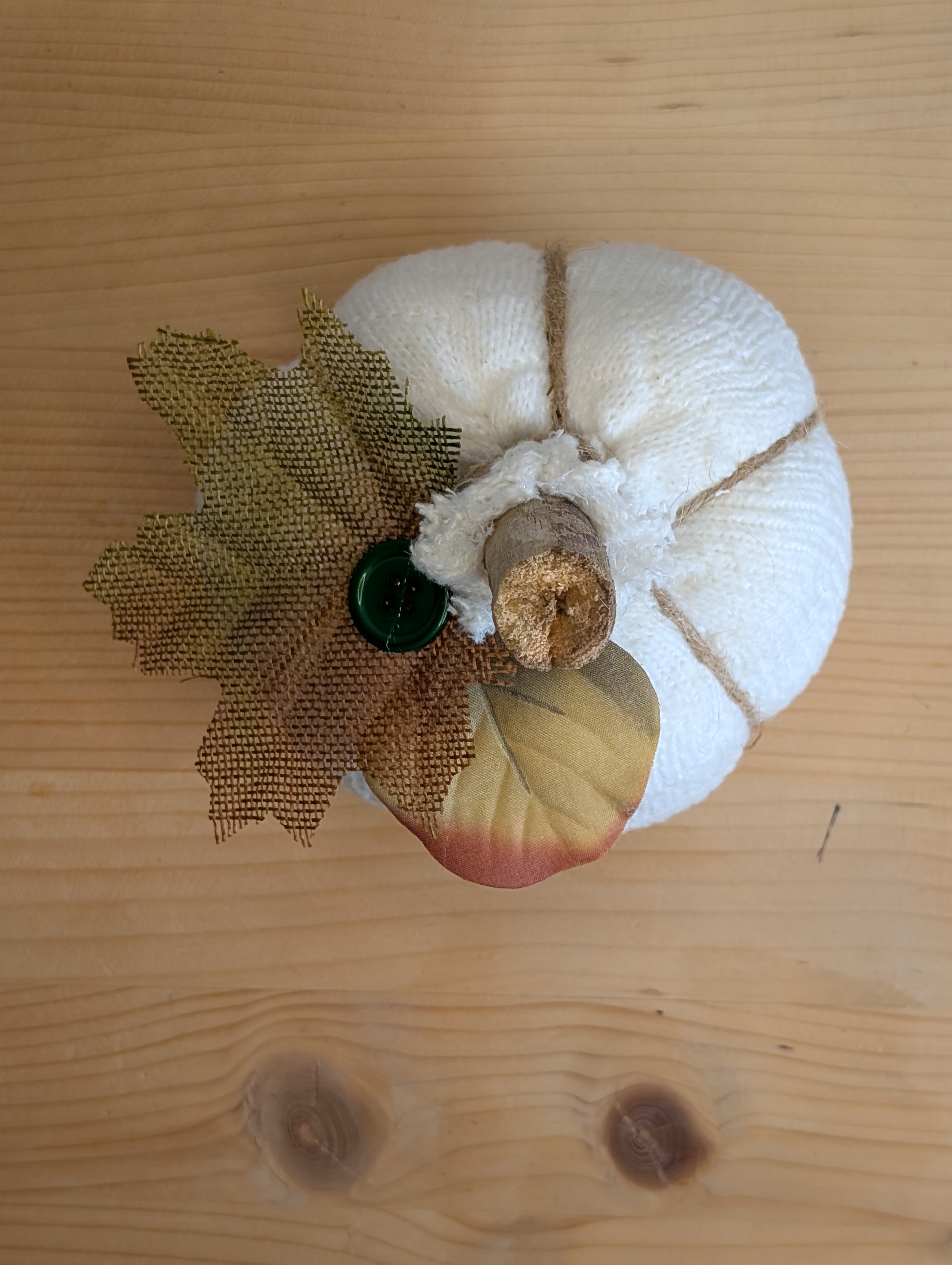 Top view of the sock pumpkin with a burlap leaf, green button, and faux leaf glued next to the stem