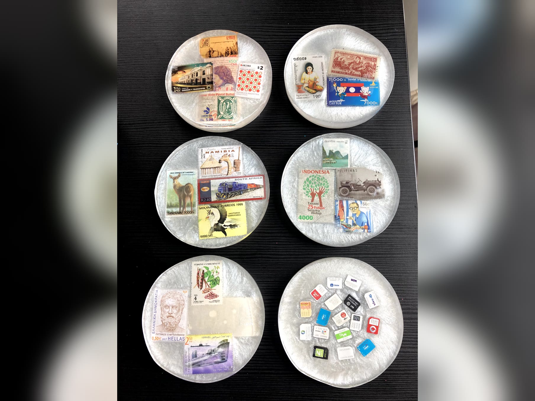 Resin coasters filled with postage stamps from around the world, plus a coaster of SIM cards, made from travel souvenirs