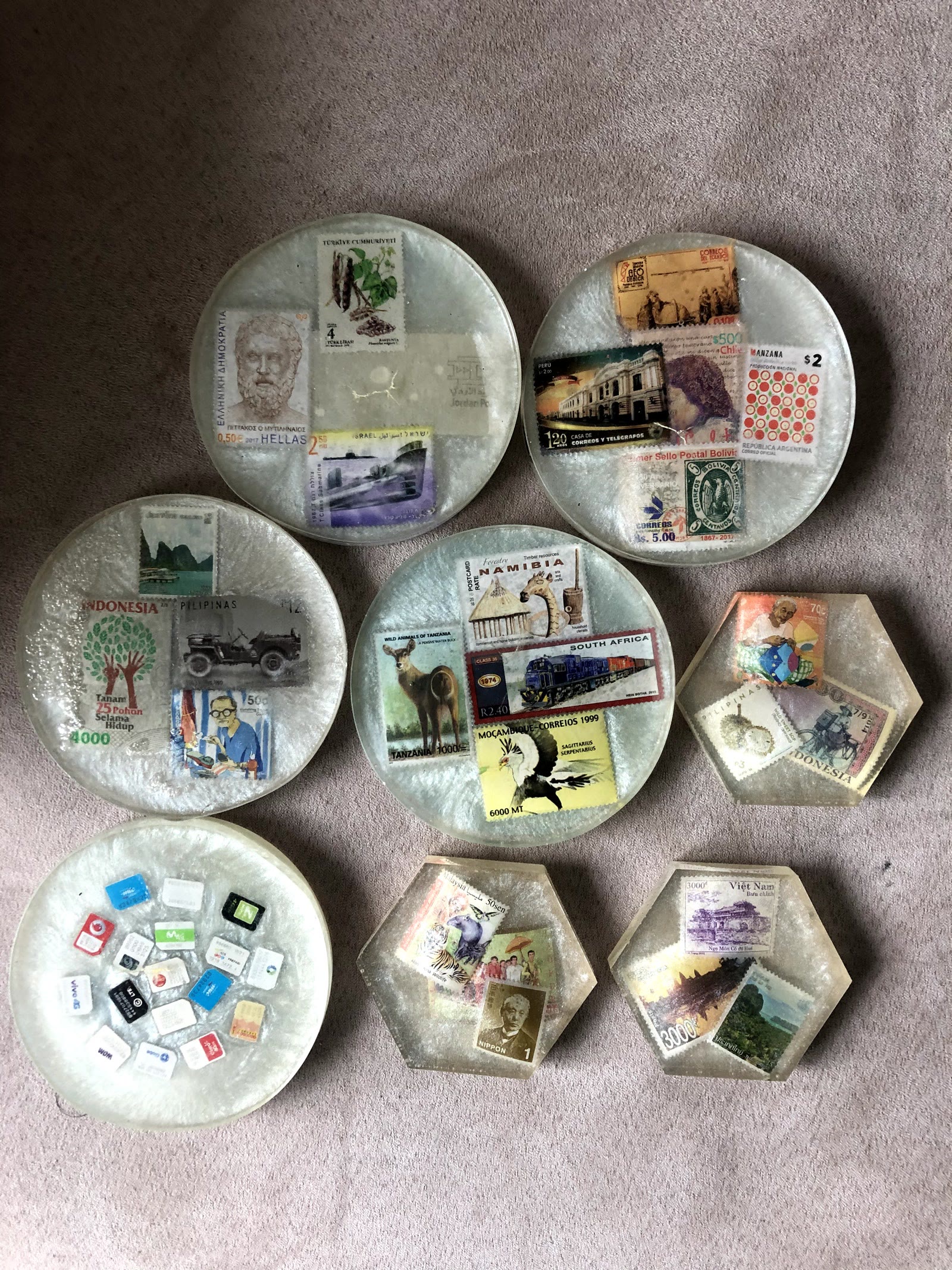 All of the resin coasters together: round and hexagon coasters with postage stamps from around the world, and one round coaster filled with SIM cards