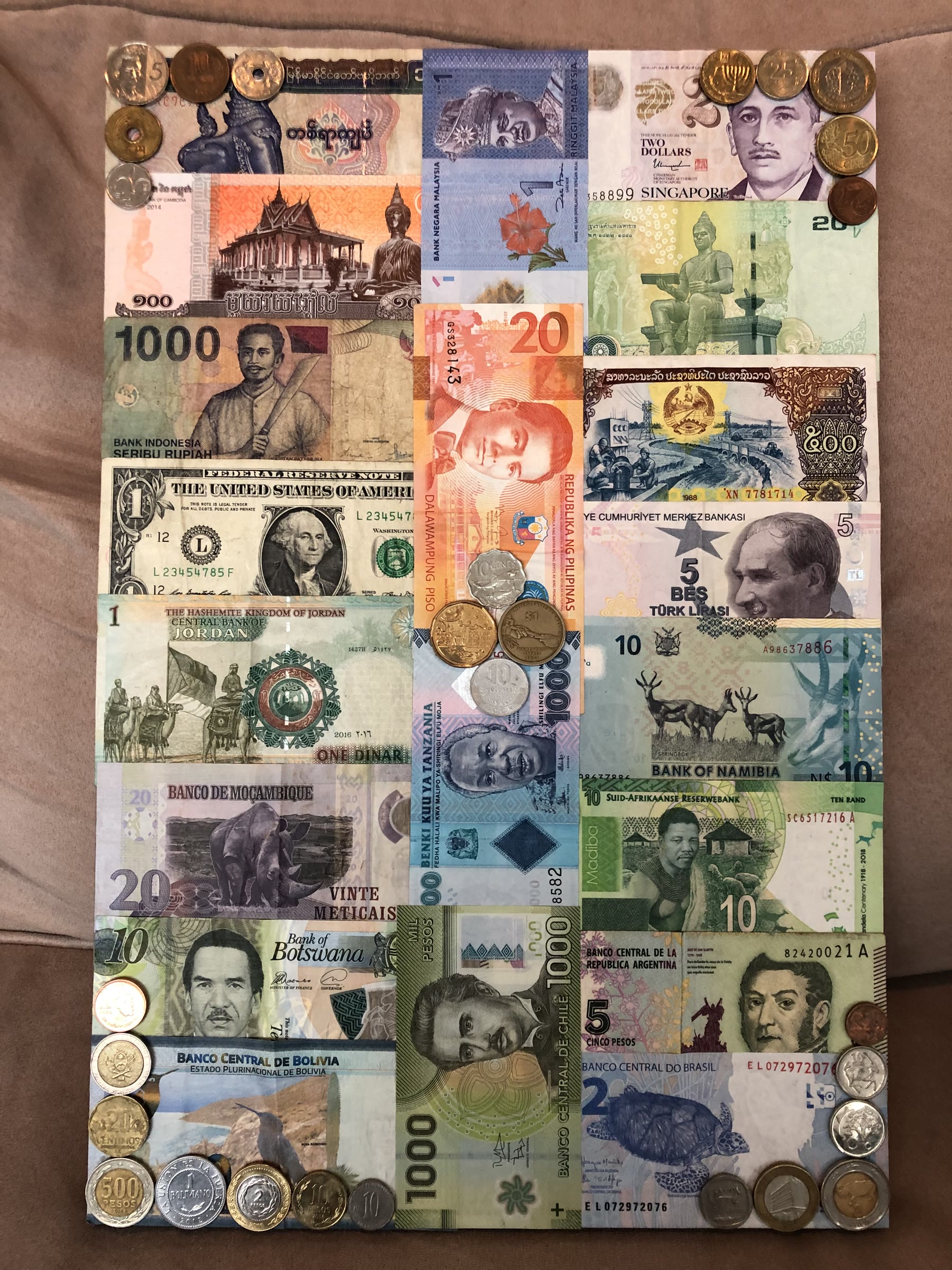 Wood panel covered in colourful paper bills from around the world, with coins hot glued along the edges, including currency from Myanmar, Cambodia, Malaysia, Singapore, Laos, Indonesia, the Philippines, Turkey, Jordan, Tanzania, Namibia, Mozambique, South Africa, Botswana, Bolivia, Chile, Argentina and Brazil
