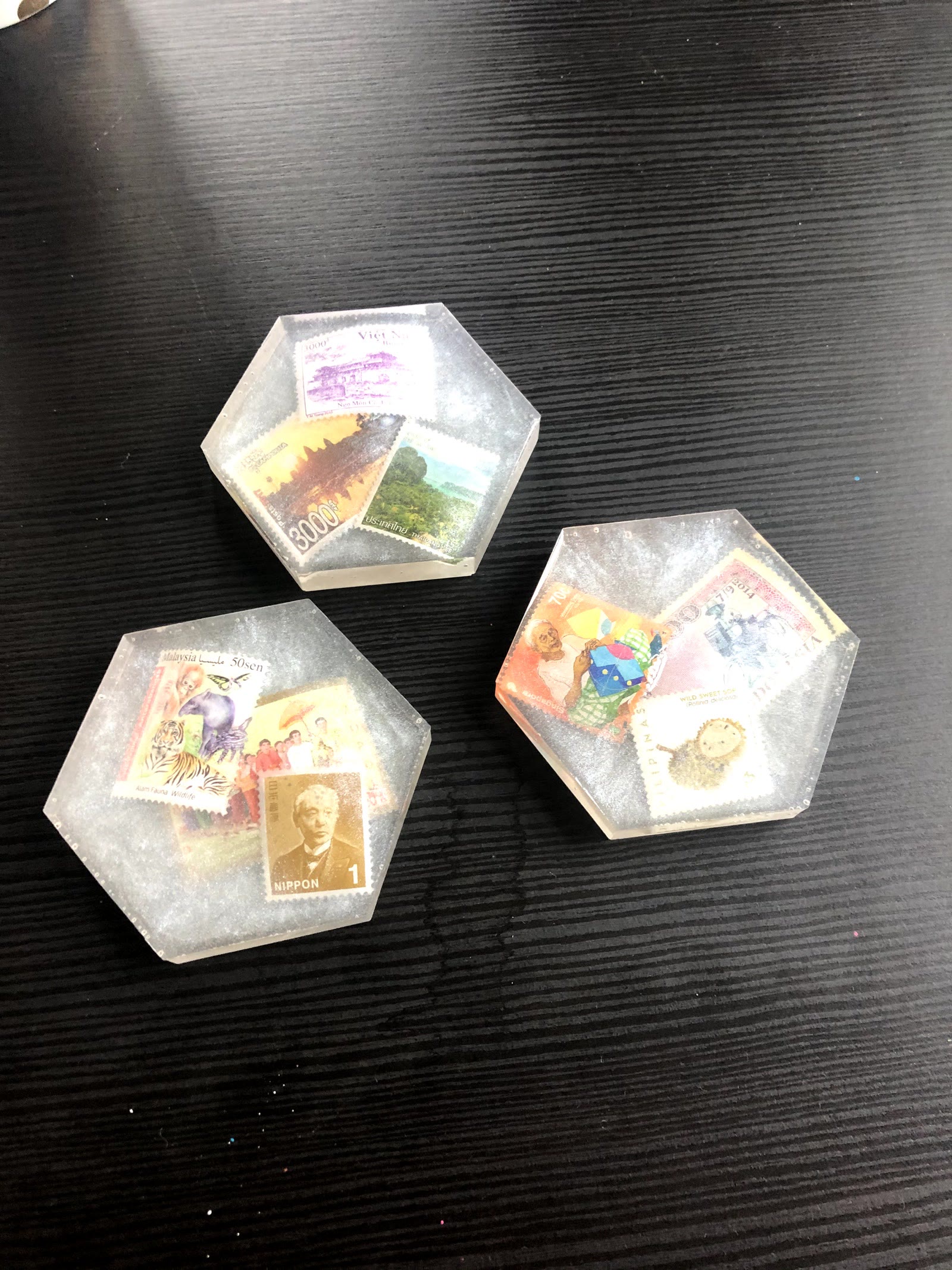 Three finished hexagon resin coasters with glittery grey resin and stamps from Vietnam, Cambodia, Thailand, Malaysia, Laos, Japan, Singapore, Indonesia and the Philippines